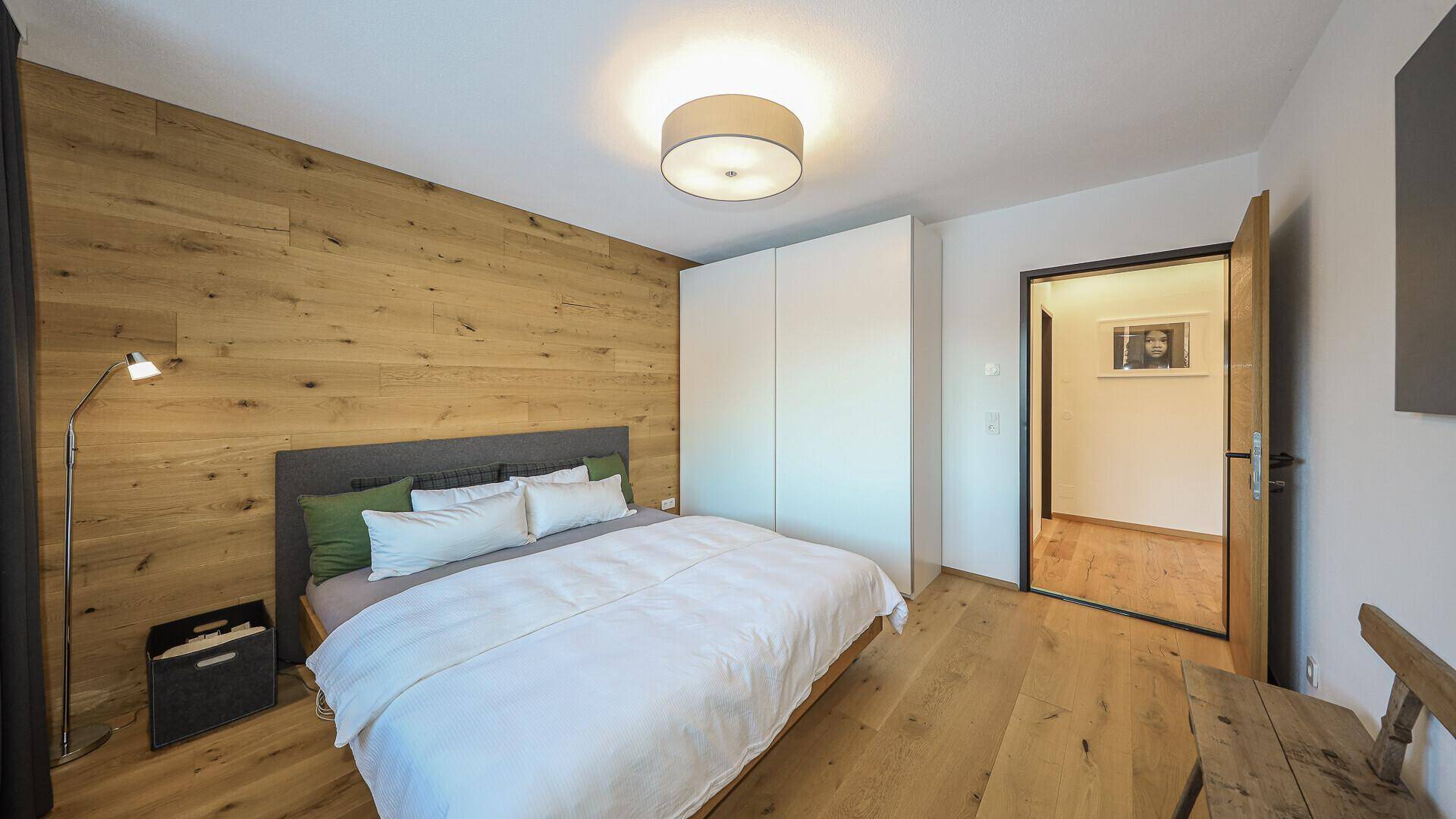 Schlafzimmer mit Holzwand, Einbauschränken und Zugang zu einem weiteren Raum.