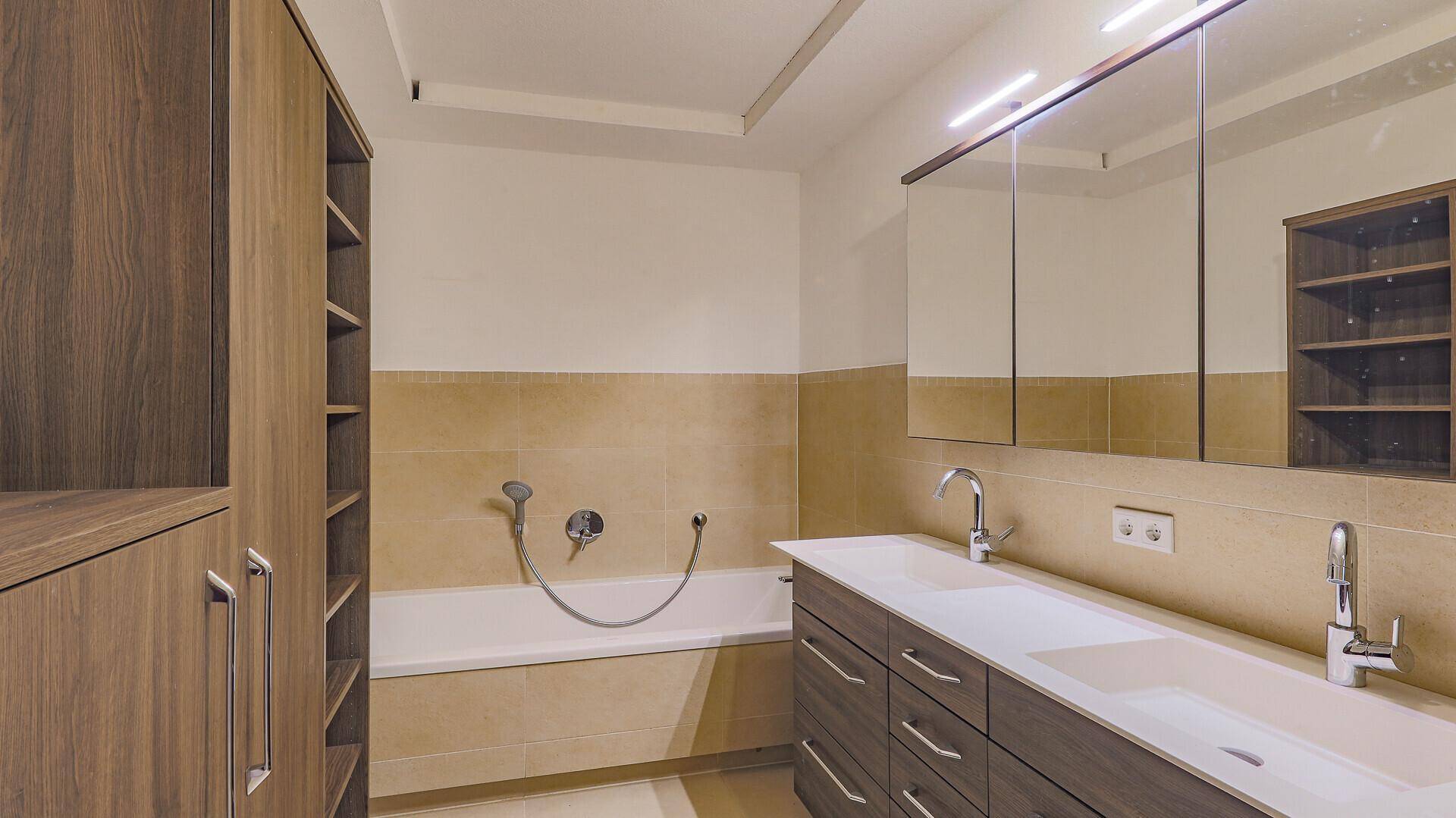 Geräumiges Badezimmer mit Doppelwaschbecken, Badewanne und praktischen Einbauschränken.