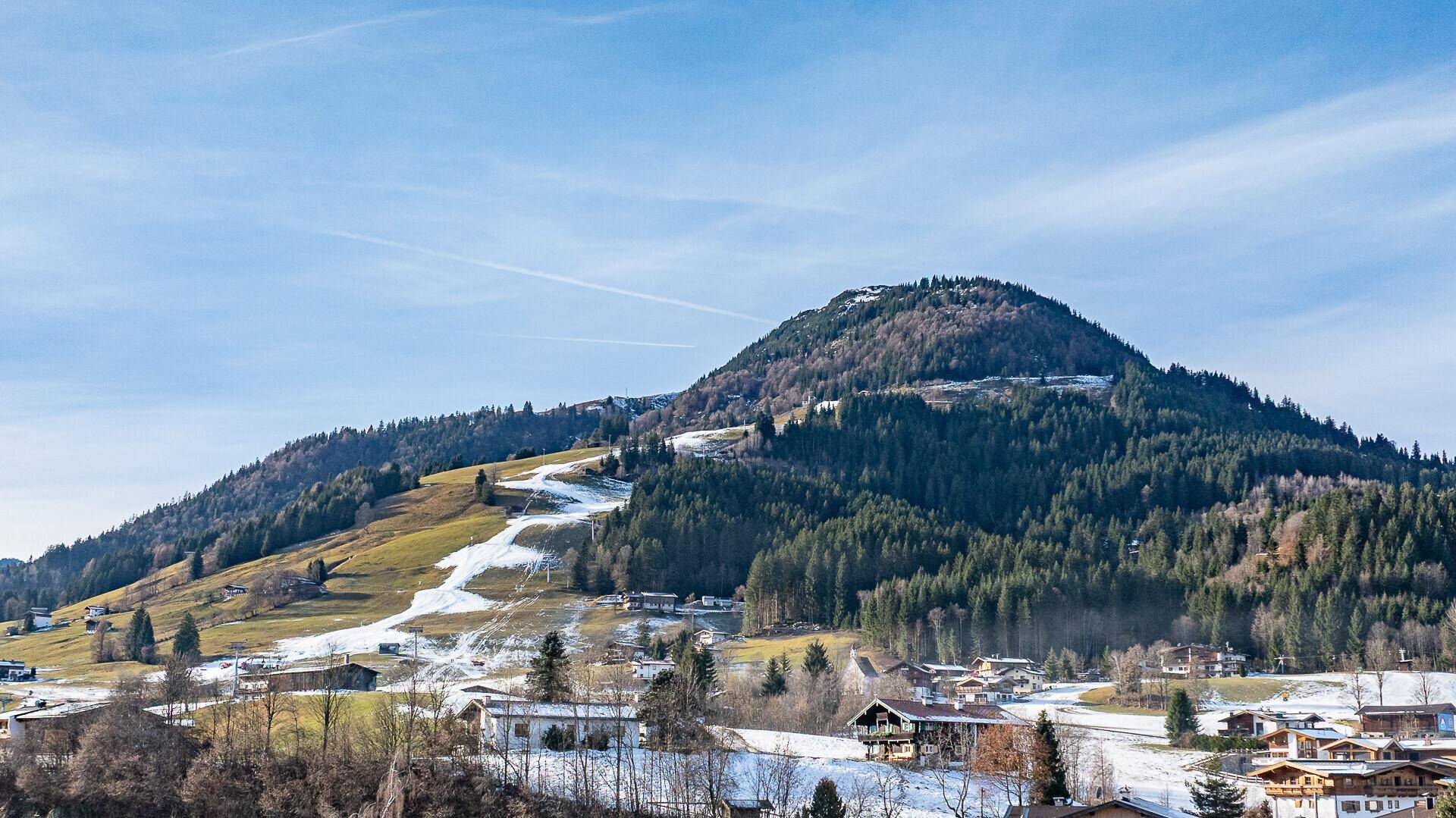 Weitläufige Berglandschaft mit teilweise schneebedeckten Hängen und dichten Wäldern.