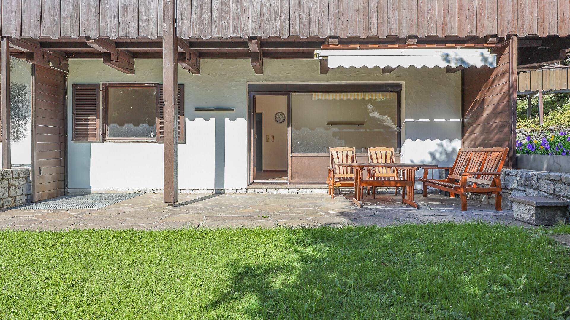 Gemütliche Terrasse mit Holzmöbeln und direktem Zugang zu einer gepflegten Rasenfläche.
