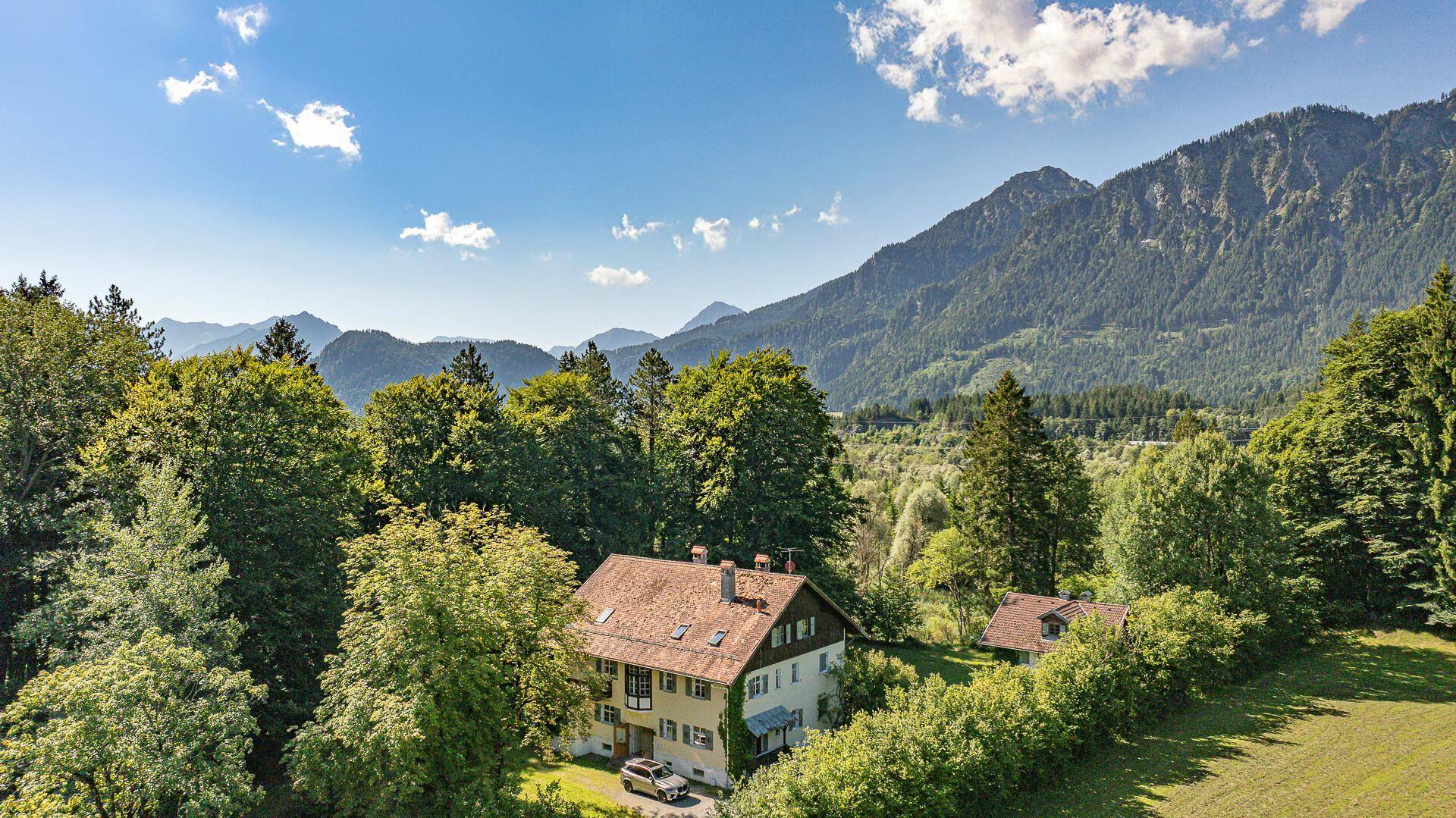 Weitläufige Luftaufnahme des Anwesens, eingebettet in grüne Wälder mit beeindruckendem Bergblick.