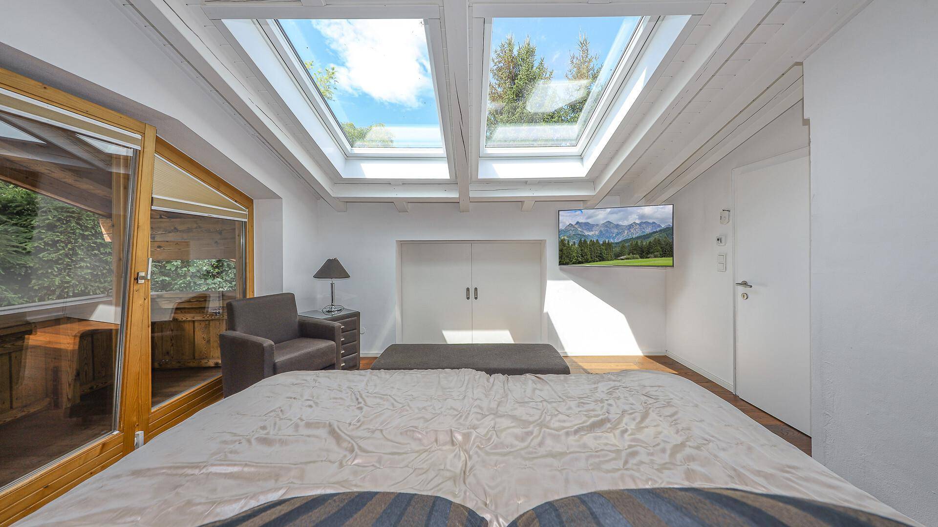 Lichtdurchflutetes Schlafzimmer mit mehreren Dachfenstern und Bergblick auf dem Fernseher.