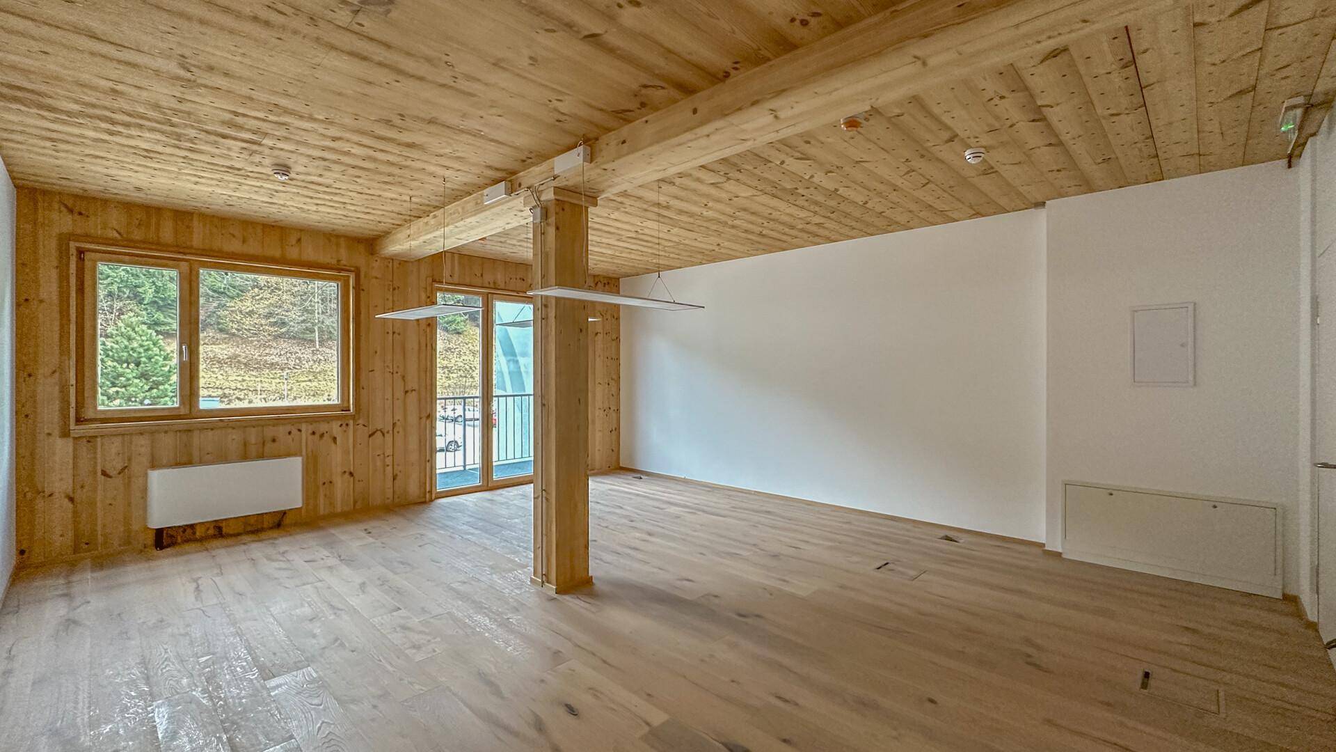 Heller Raum mit Holzboden, Holzwänden und einer Holzbalkendecke, inklusive Zugang zum Balkon.
