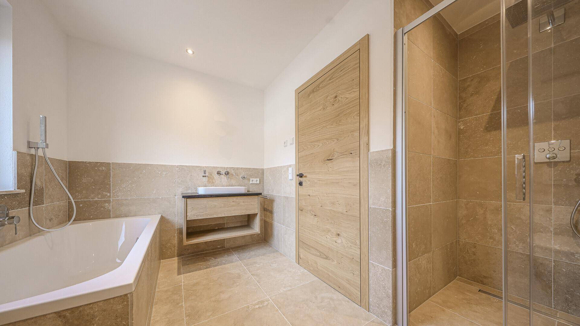 Modernes Badezimmer mit Badewanne, Dusche und beigefarbenen Fliesen.