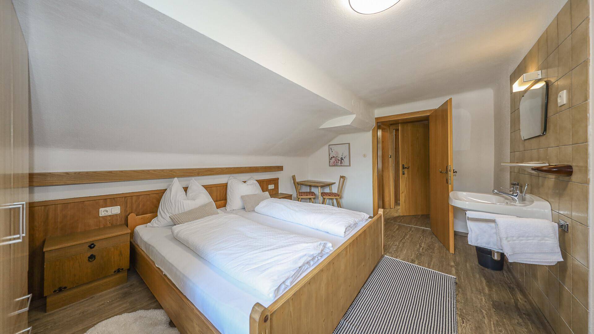 Helles Dachgeschoss-Schlafzimmer mit schräger Decke, Doppelbett und integriertem Waschbecken.