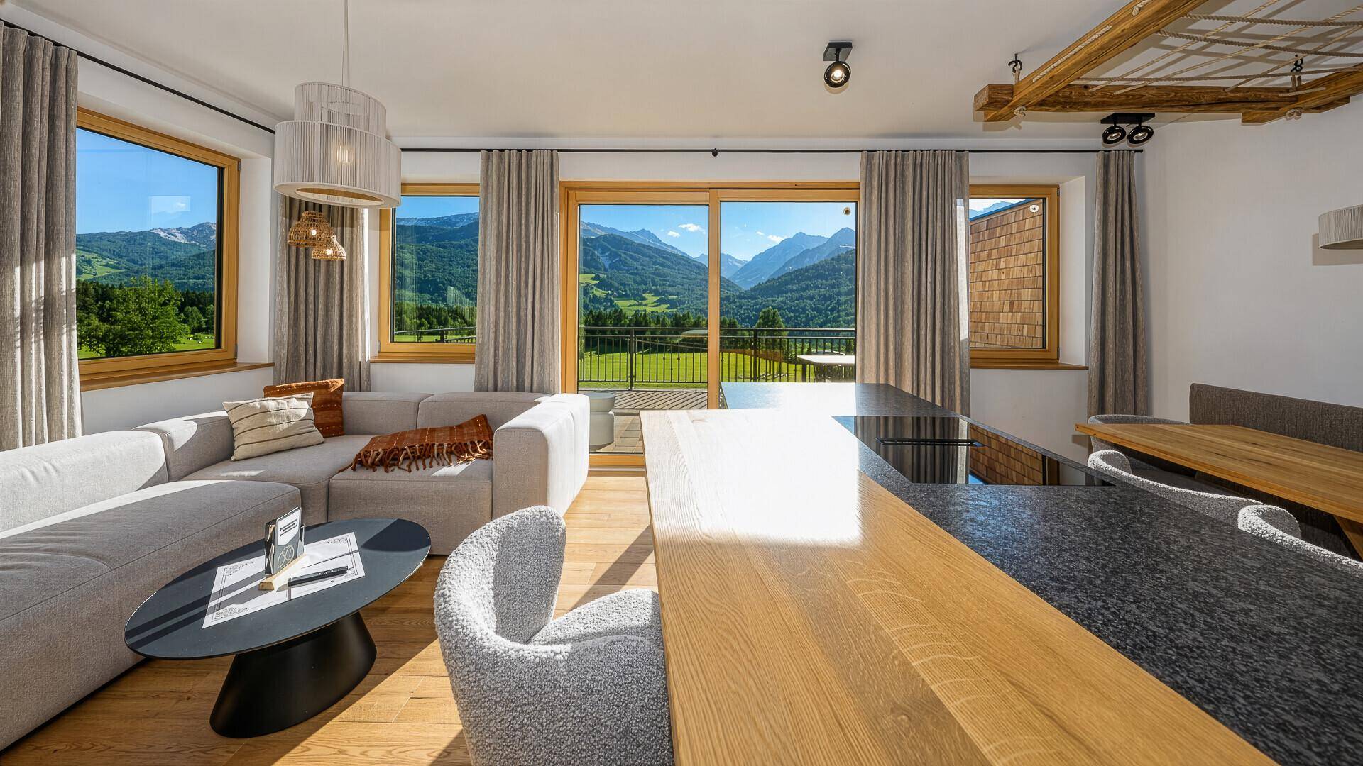 Lichtdurchfluteter Wohnbereich mit großem Sofa, Kücheninsel und weitem Bergblick durch Panoramafenster.