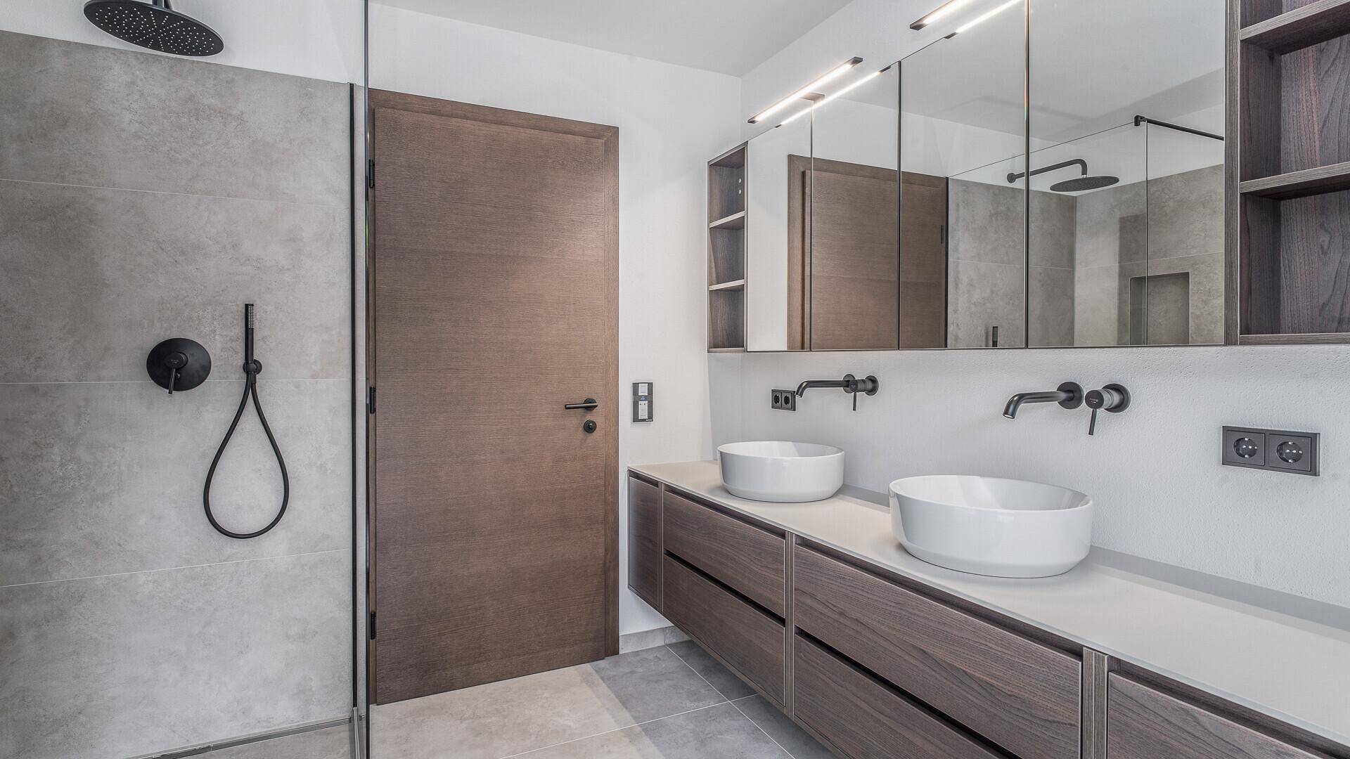 Elegantes Badezimmer mit zwei Aufsatzwaschbecken, großer begehbarer Dusche und modernen Armaturen.