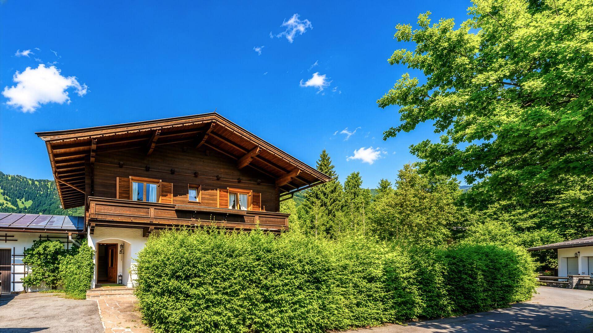 Charmantes Chalet mit gepflegter Hecke und traditioneller Holzfassade vor Bergkulisse.