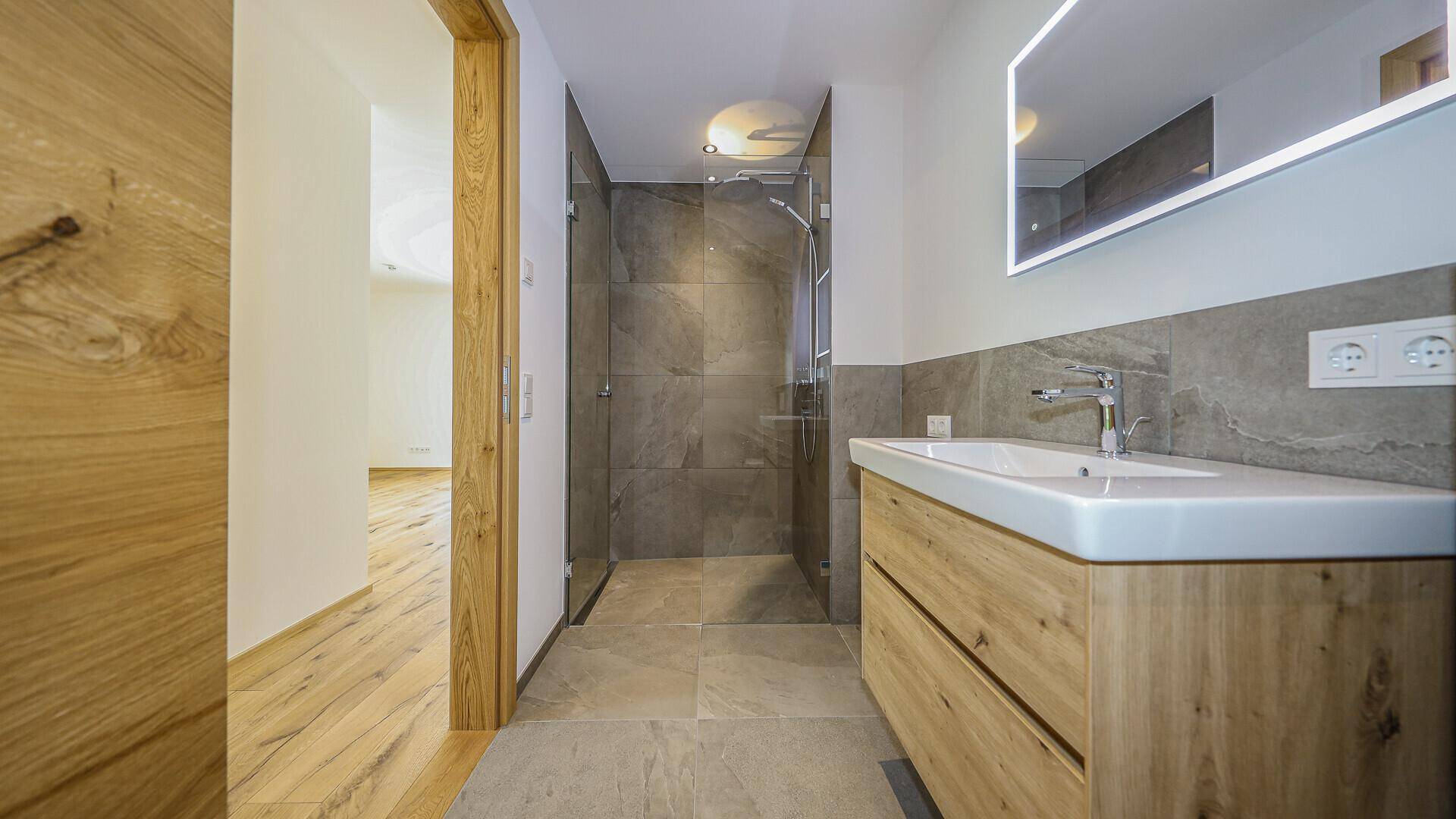 Modernes Badezimmer mit begehbarer Dusche, Holzwaschtisch und großformatigen Fliesen.