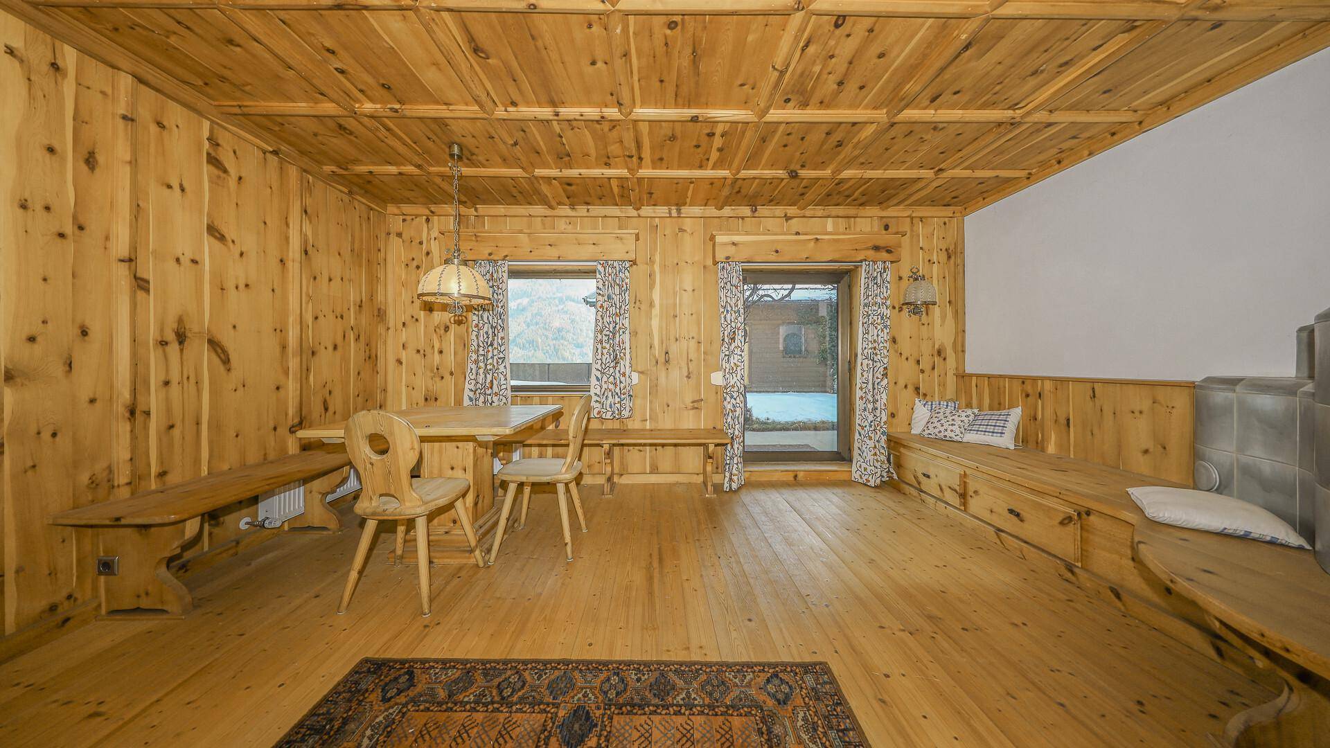 Rustikaler Wohn-Essbereich mit Holzdielenboden, Holzbänken und einem traditionellen Kachelofen.