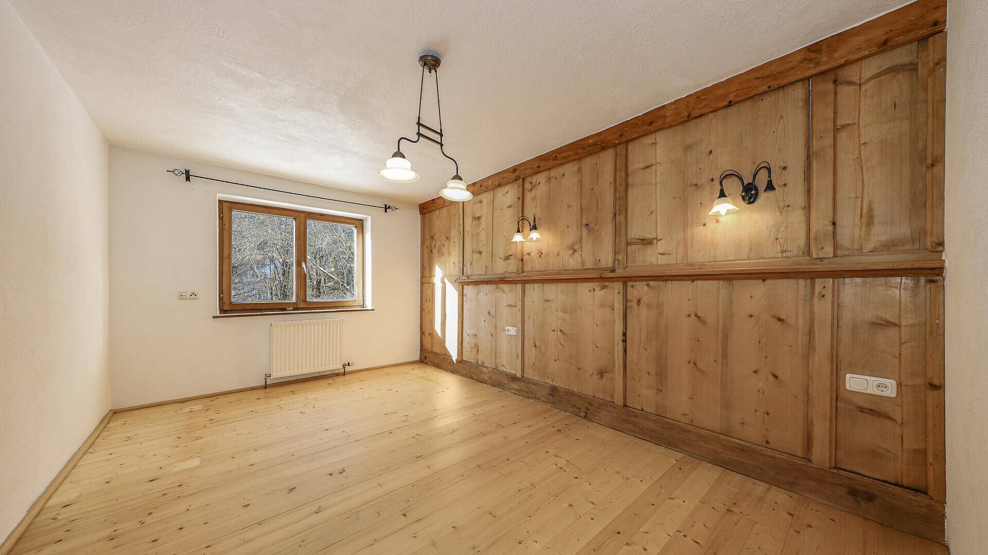 Helles Zimmer mit Holzvertäfelung, Holzboden und Blick ins Grüne.