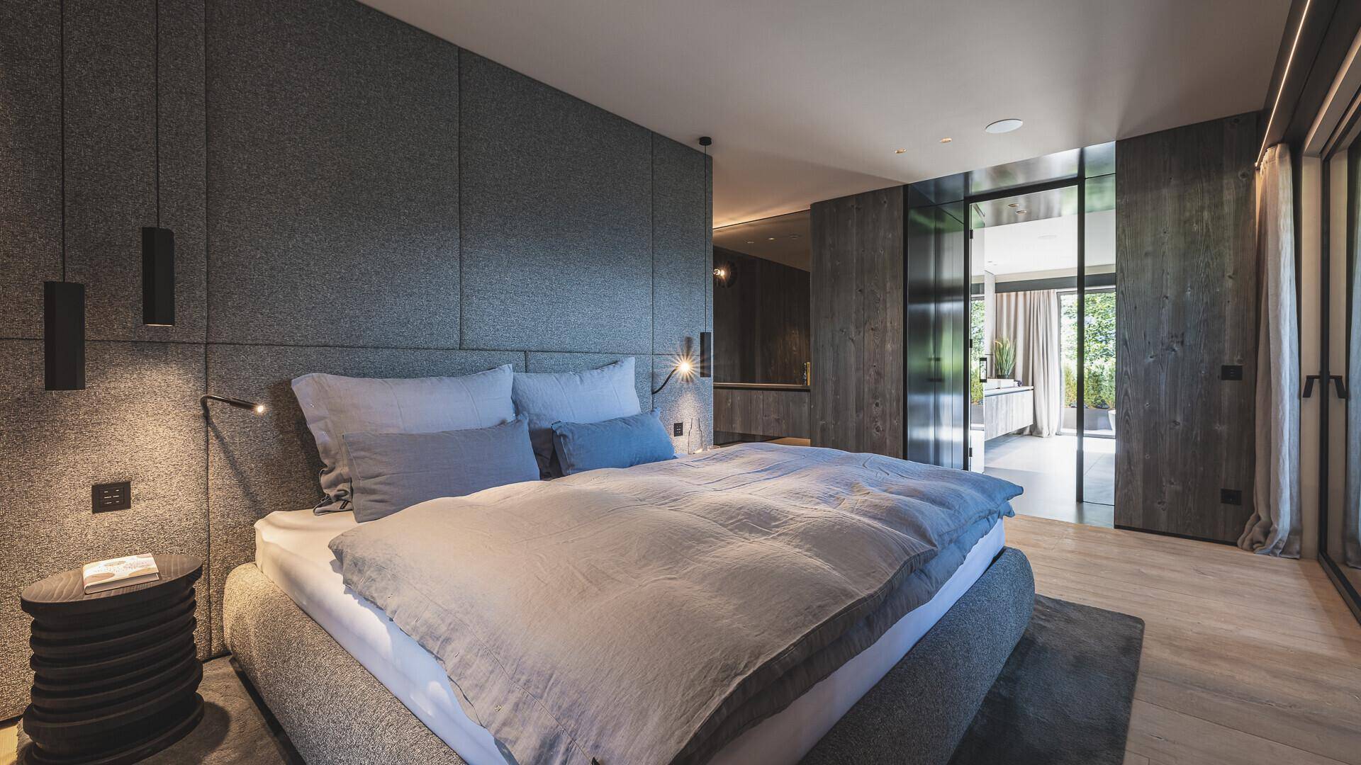 Modernes Schlafzimmer mit dunklen Akzentwänden, Holzboden und Zugang zur Terrasse.