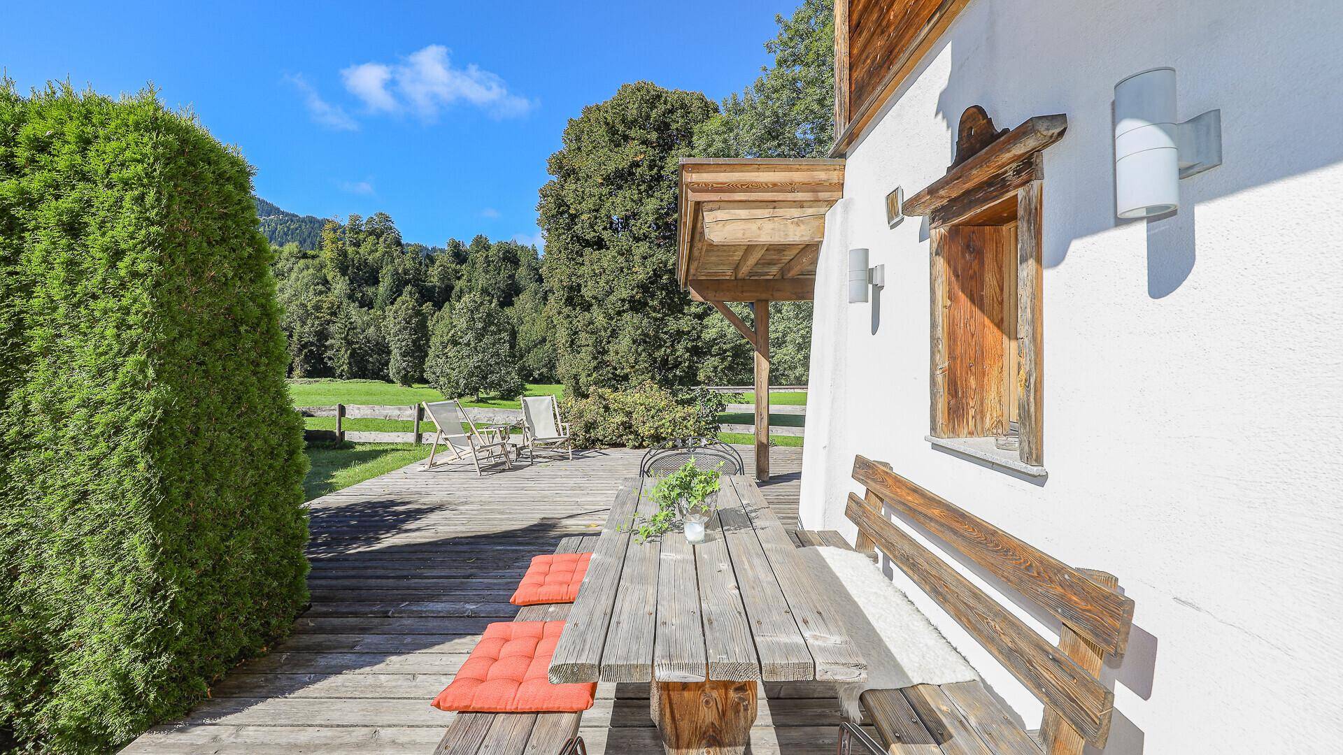 Große Holzterrasse mit Esstisch und Liegestühlen, umgeben von Natur.