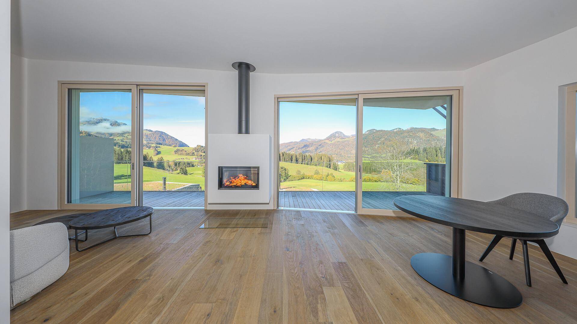 Helles Wohnzimmer mit Kamin, Holzboden und großen Schiebetüren zur Terrasse mit Bergblick.