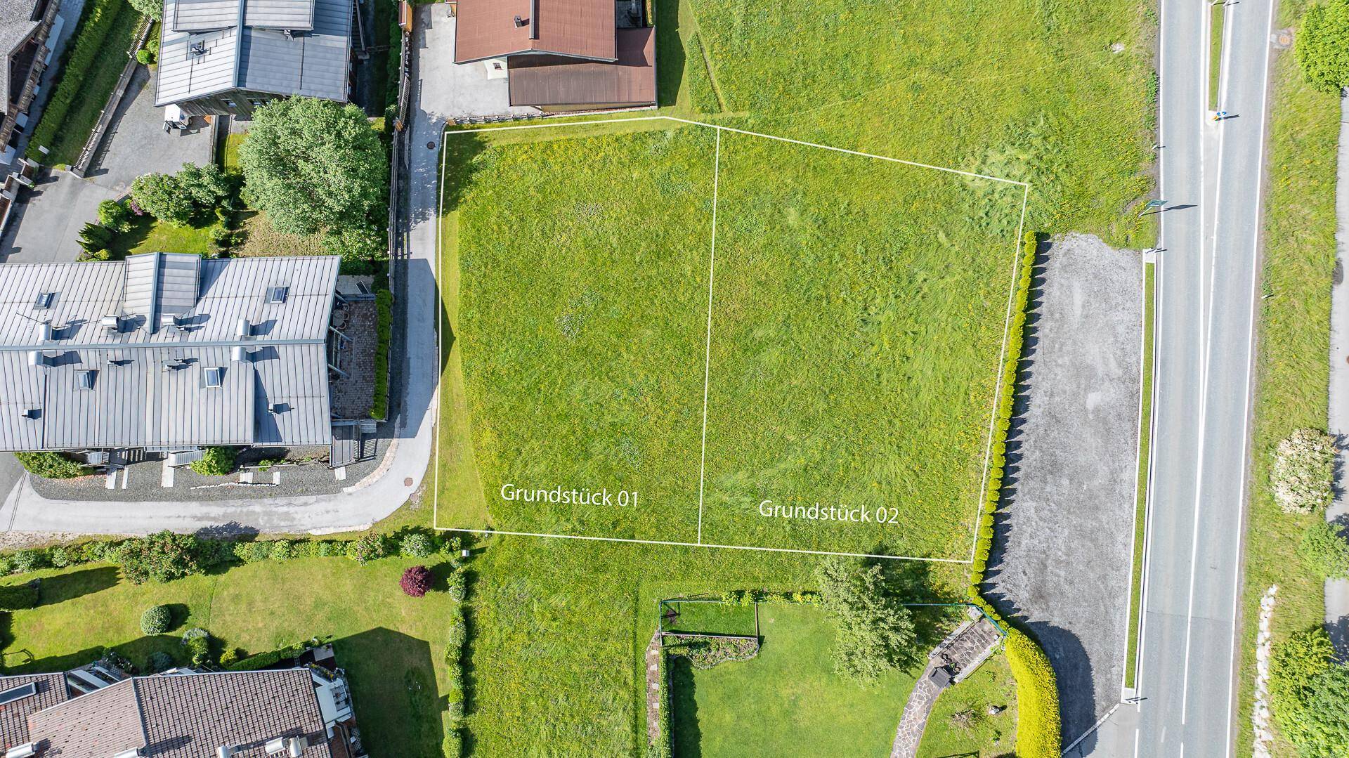 Luftaufnahme von zwei nebeneinander liegenden Grundstücken, umgeben von Grünflächen und einer Straße.