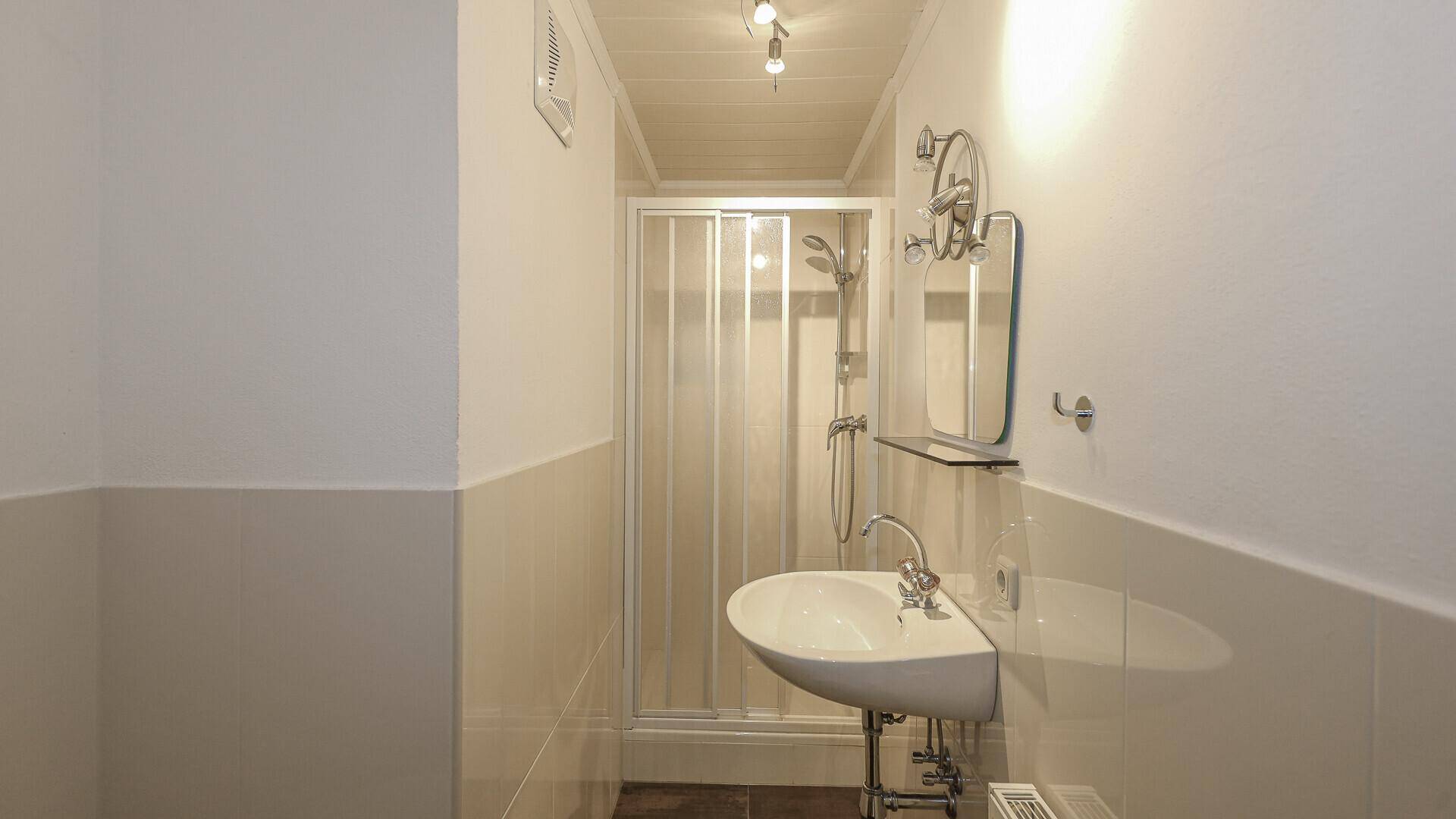 Kleines Badezimmer mit Dusche, Einzelwaschbecken und hellen Fliesen.