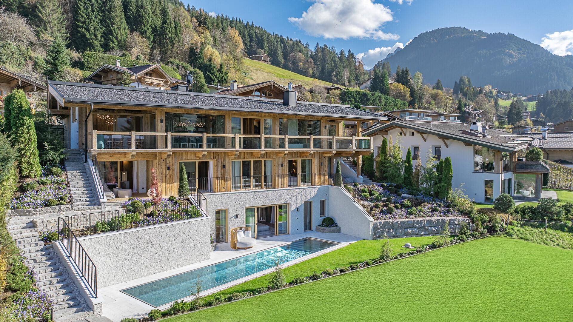 Elegantes Anwesen mit weitläufigem Garten, Pool und atemberaubendem Bergblick unter blauem Himmel.