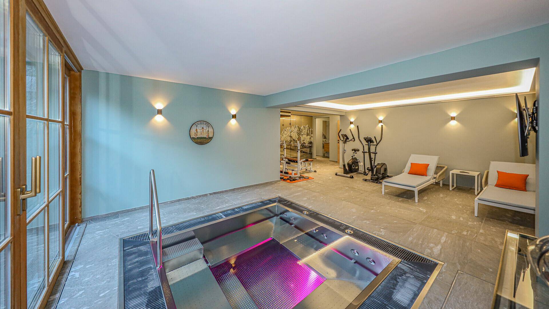 Wellnessbereich mit Whirlpool, Fitnessgeräten und großen Fenstern für viel Tageslicht.