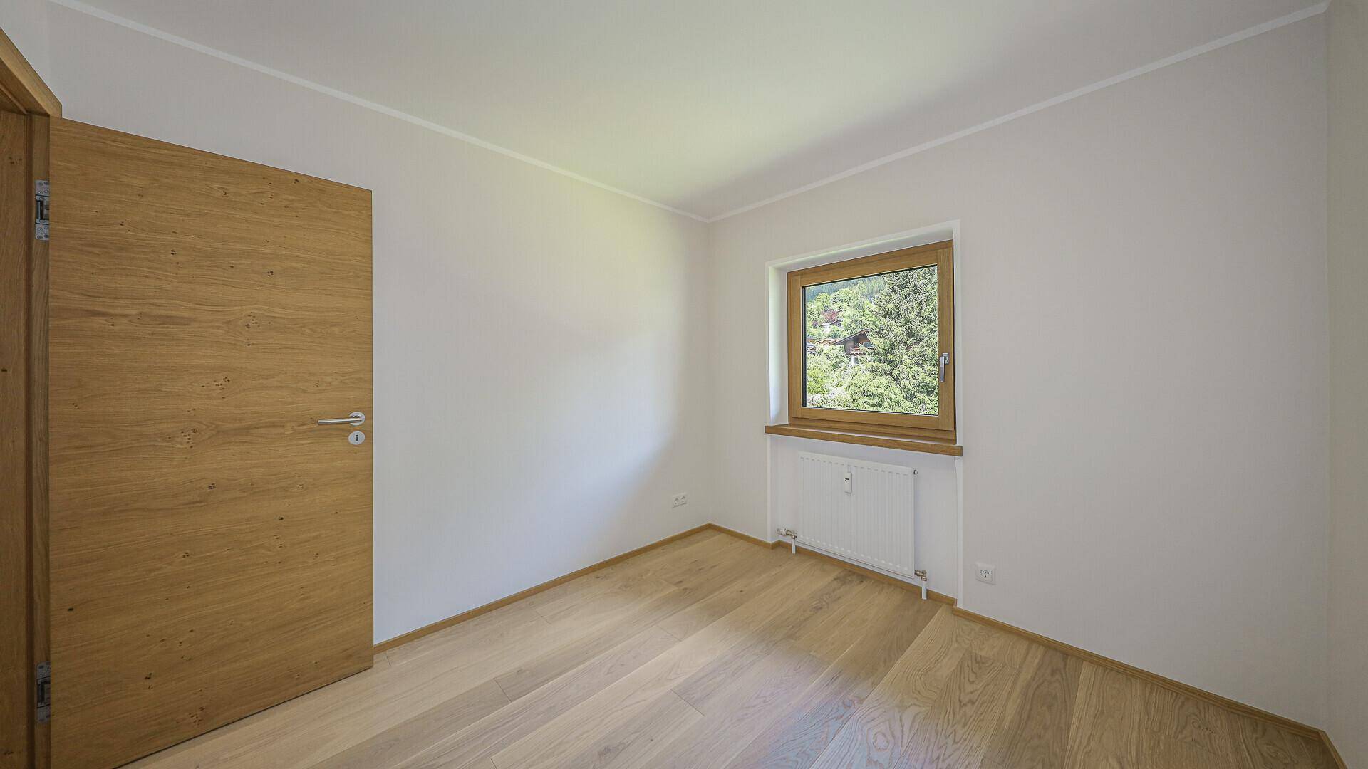 Helles Zimmer mit Holzboden und Fenster, ideal als Kinderzimmer oder Gästezimmer nutzbar.