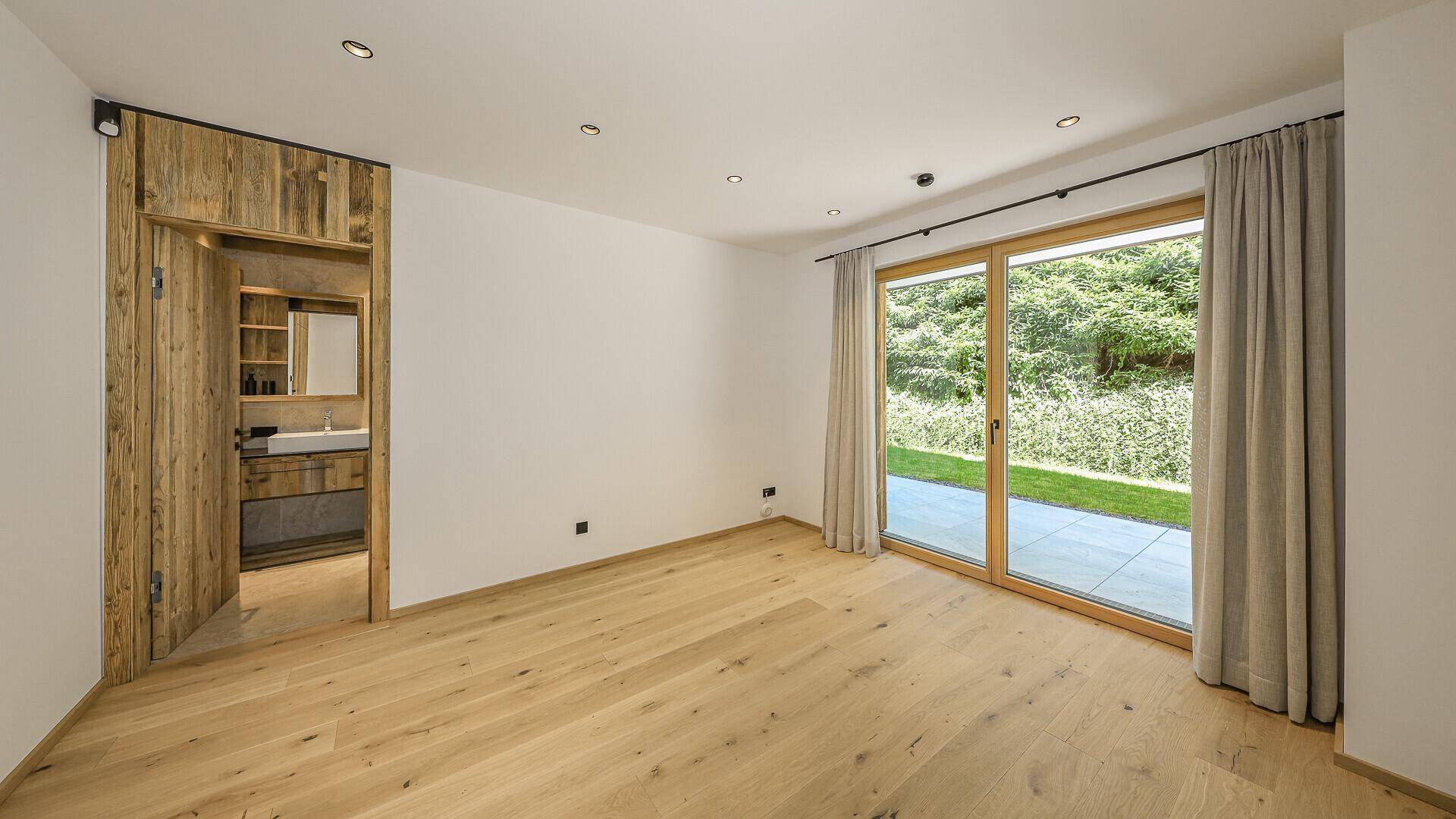 Geräumiges Zimmer mit Holzboden und großen Schiebetüren zum Gartenbereich.