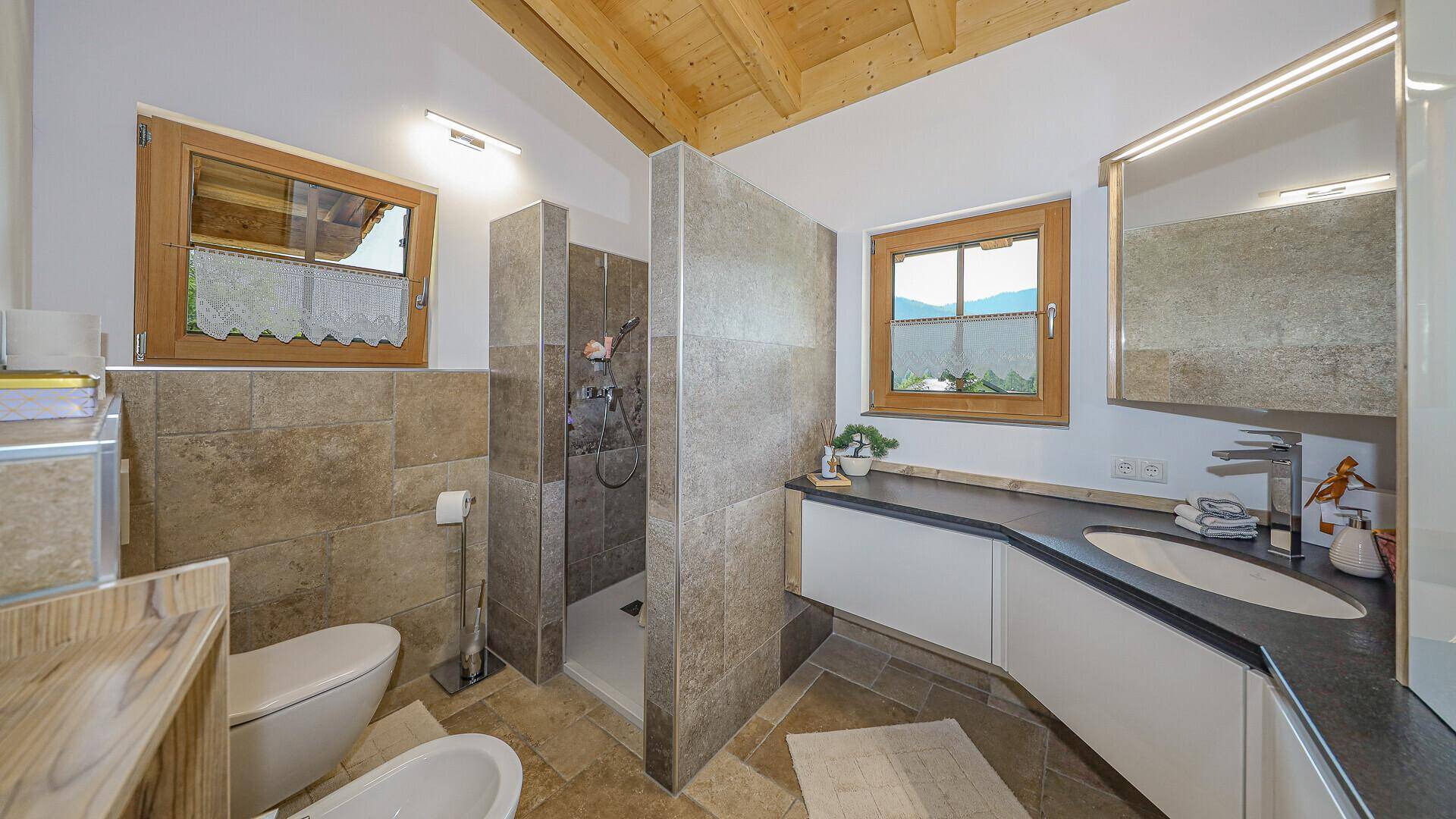 Modernes Badezimmer mit begehbarer Dusche, Einzelwaschbecken, Bidet und zwei Fenstern für Tageslicht.