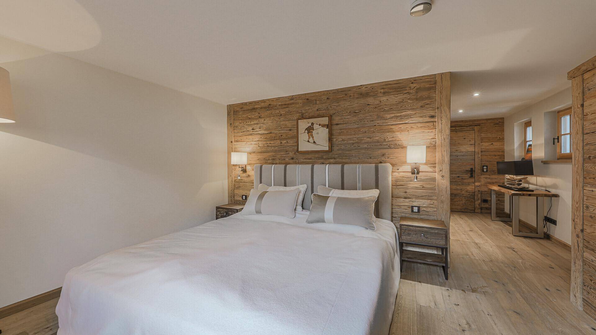 Geräumiges Schlafzimmer mit Holzwand, Doppelbett und Zugang zu einem weiteren Raum.