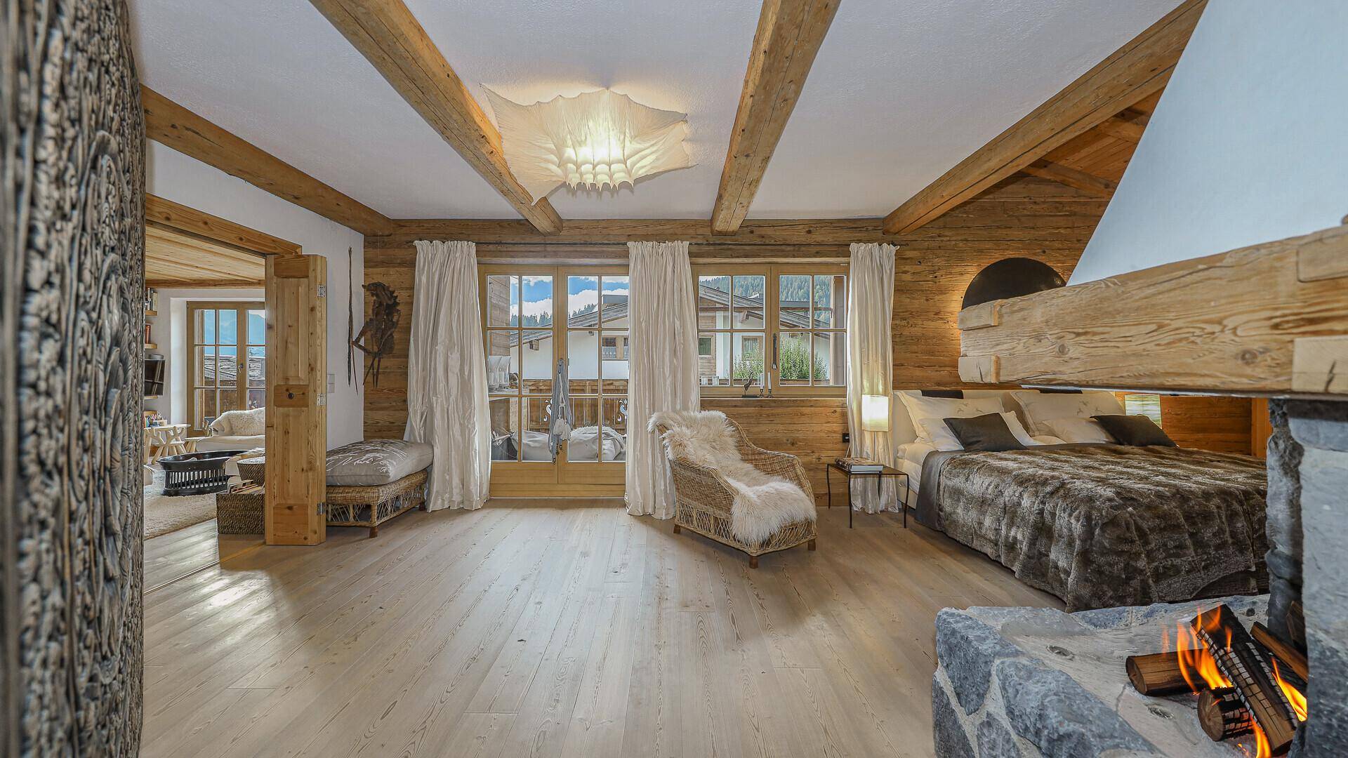 Helles Schlafzimmer mit Holzbalken, Kamin und Zugang zu einem Balkon mit schöner Aussicht.