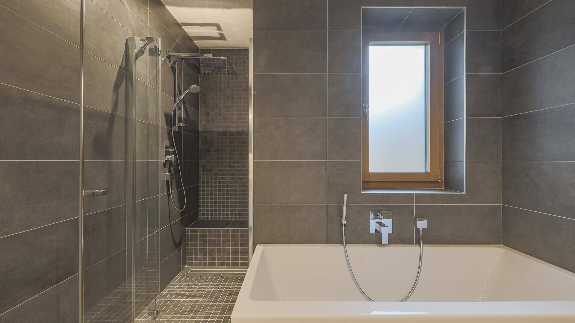 Modernes Badezimmer mit Badewanne, begehbarer Dusche und Fenster für natürliches Licht.