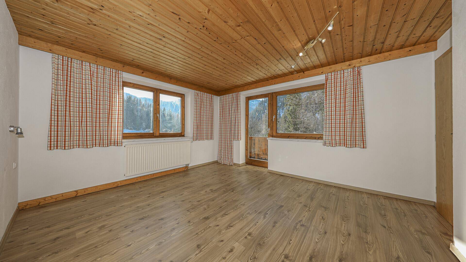 Geräumiges Zimmer mit Holzboden, Holzdecke und Fenstern mit Bergblick.