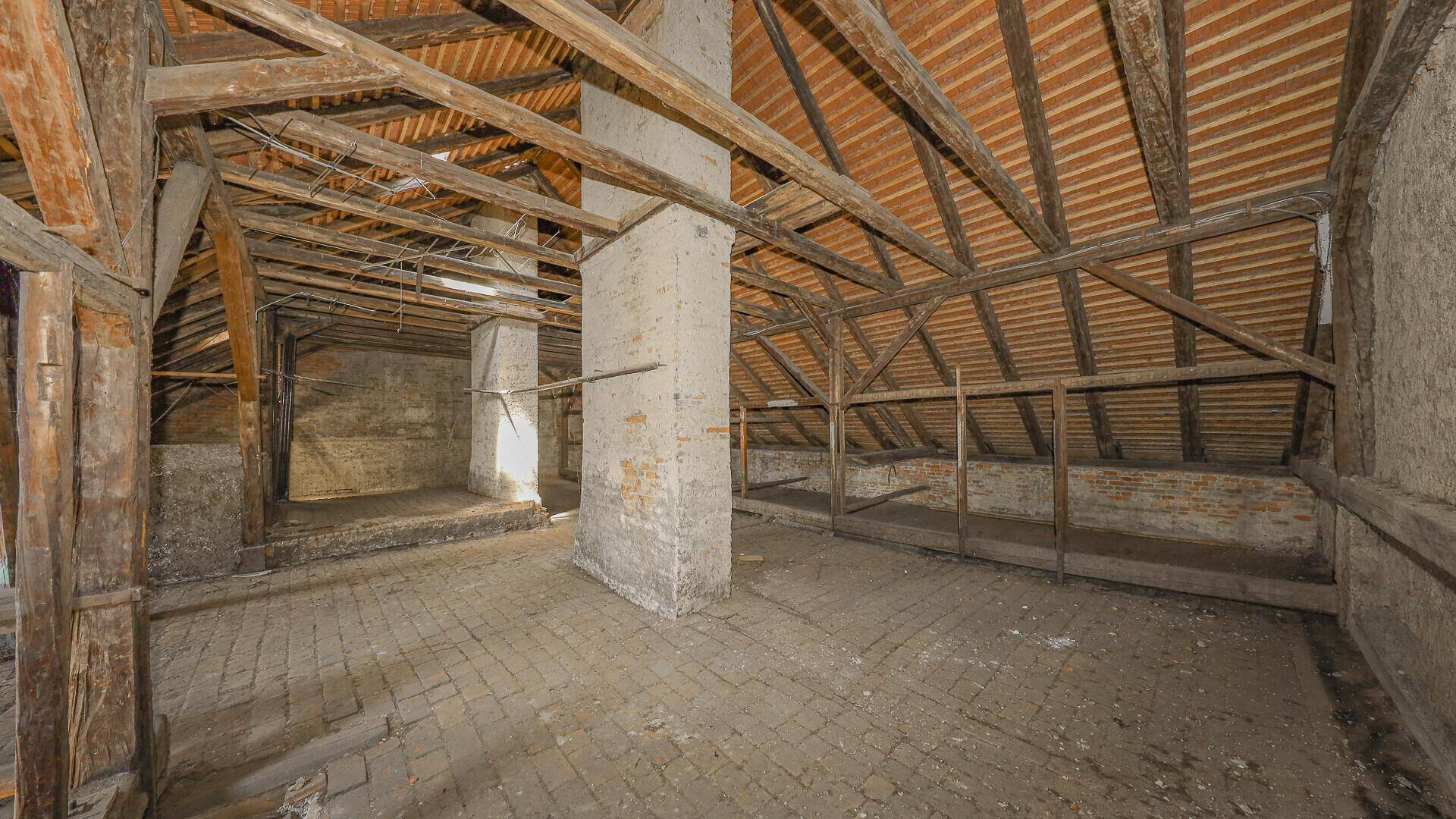 Unausgebauter Dachboden mit sichtbaren Holzbalken und Ziegelboden, bereit für den Ausbau.