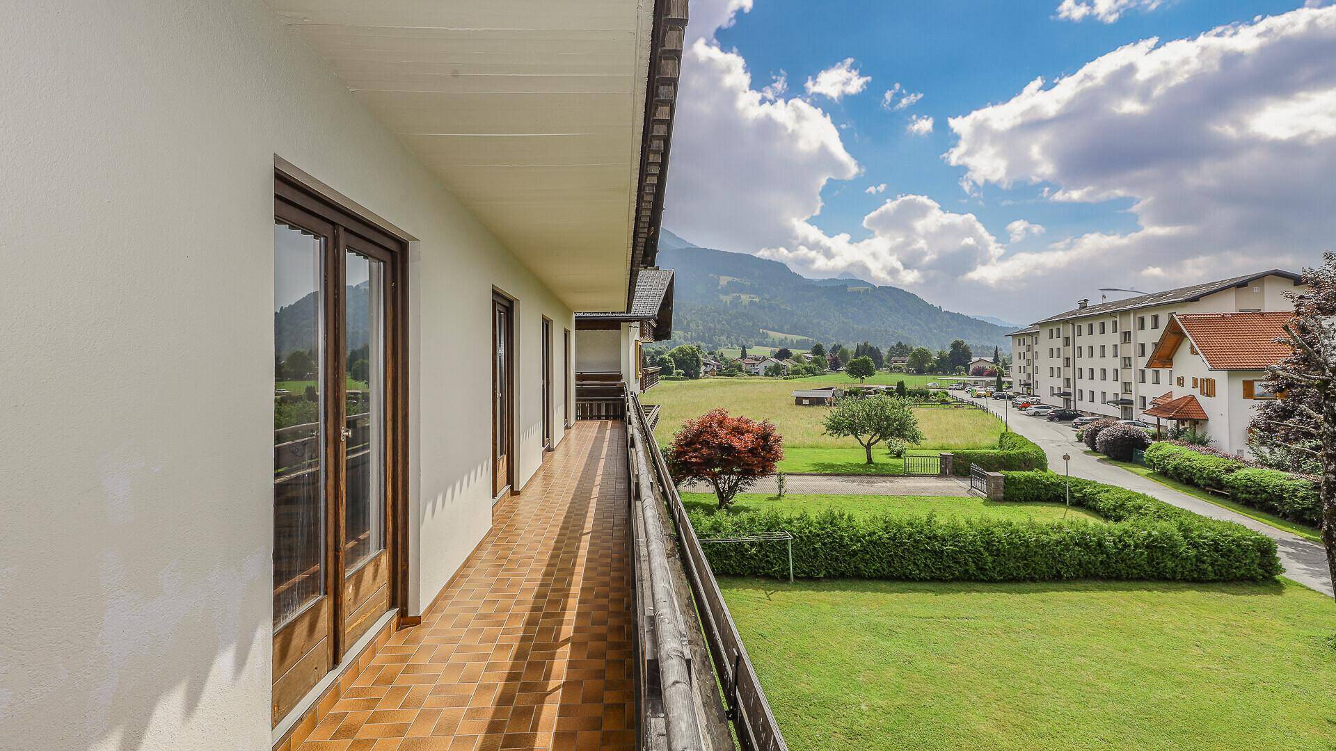 Langer Balkon mit Fliesenboden und weitem Blick über grüne Felder und Berge.