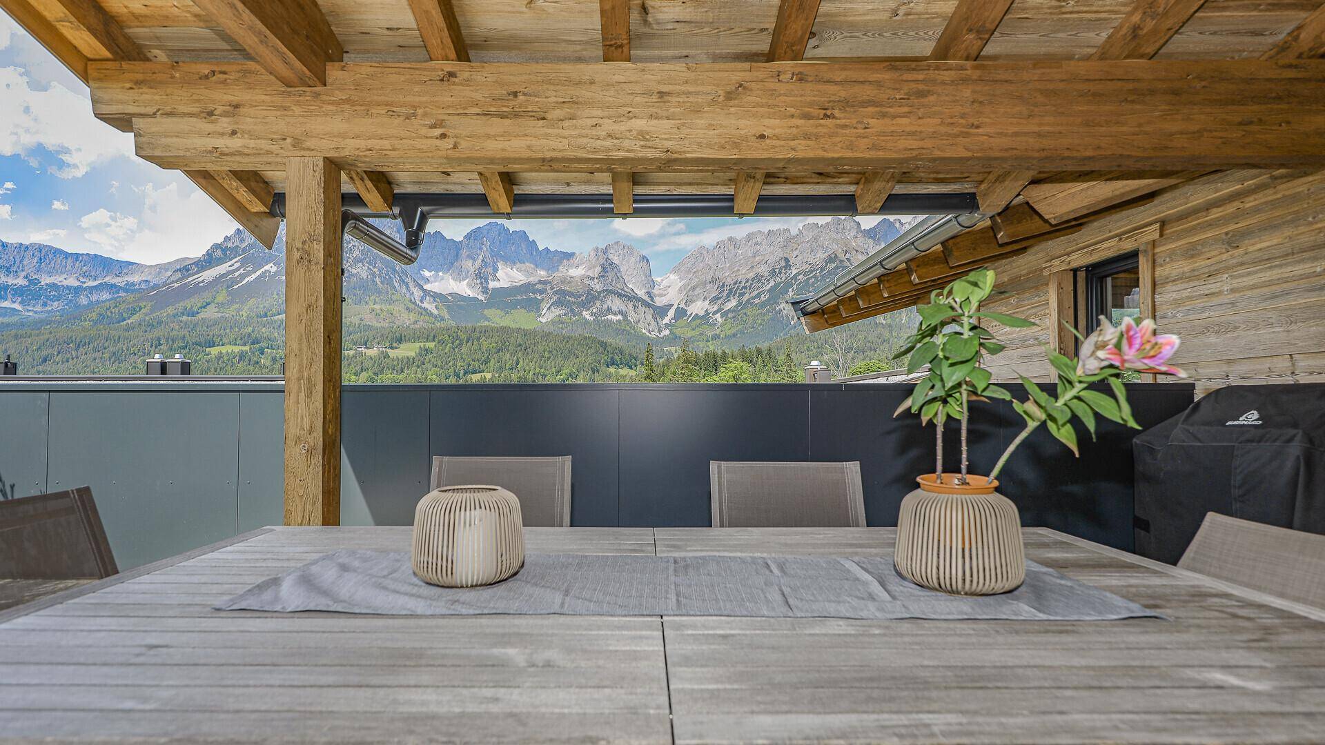 Gemütliche Terrasse mit Holztisch, Dekoration und atemberaubendem Bergblick in der Ferne.