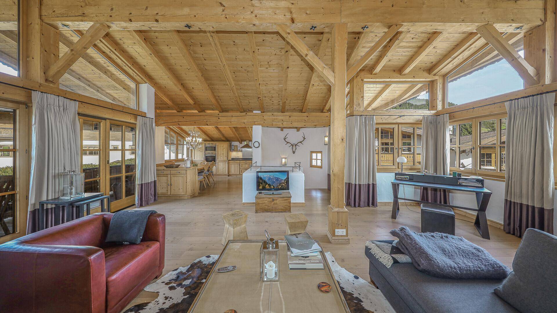 Geräumiges, lichtdurchflutetes Wohnzimmer im alpinen Stil mit Holzbalkendecke und Bergblick.