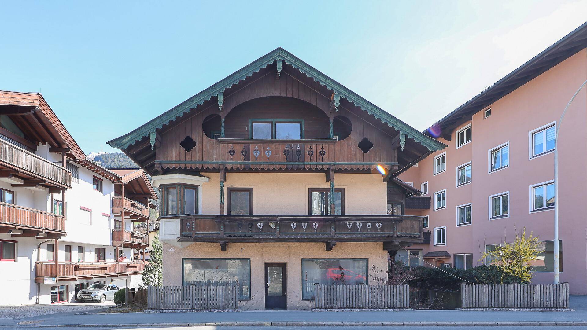 Charmantes Gebäude im traditionellen Stil mit Holzbalkonen und großen Fenstern an einer sonnigen Straße.