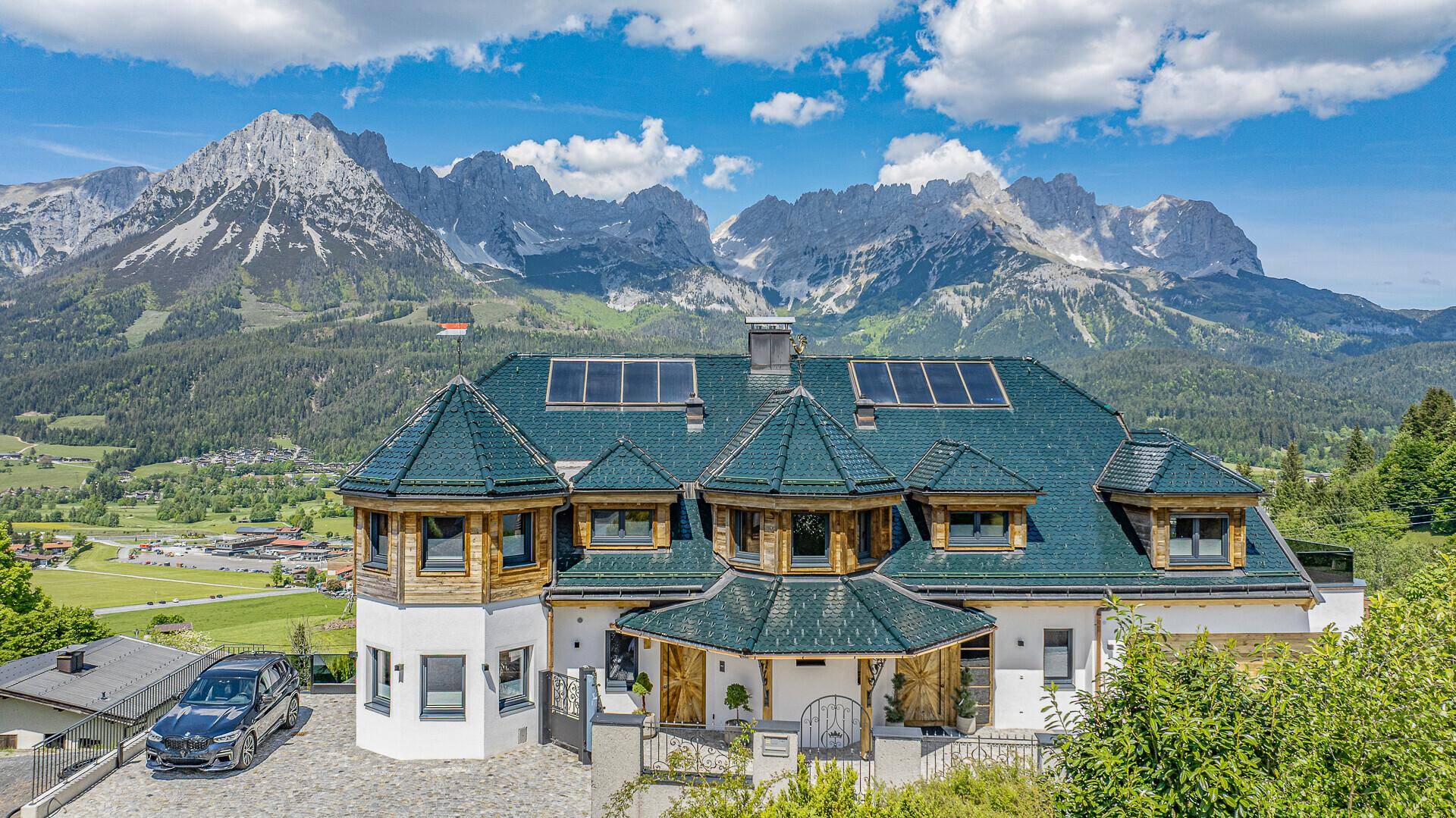 Beeindruckendes Anwesen mit grünen Dächern und Solaranlagen vor majestätischer Bergkulisse.
