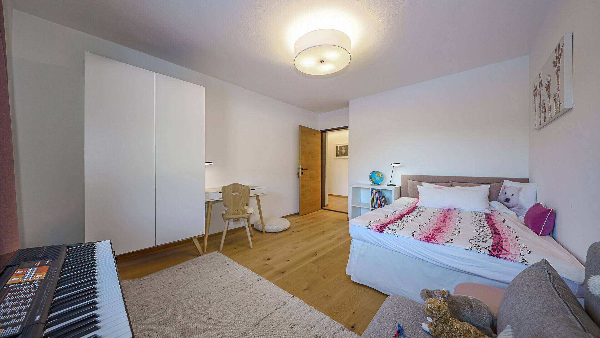 Helles Kinderzimmer mit Bett, Schreibtisch und weißem Kleiderschrank.