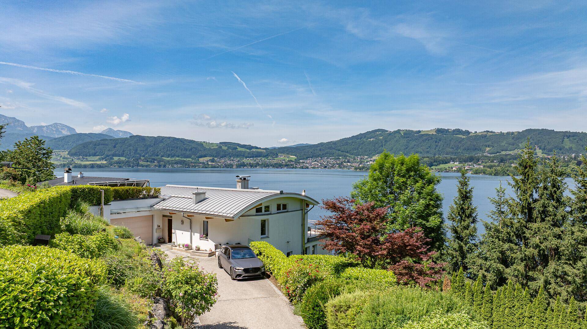 Die Villa ist eingebettet in eine grüne Hügellandschaft mit weitem Blick auf den See und die Berge.