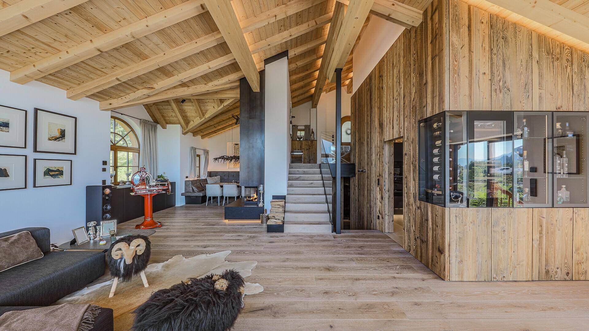 Offener Wohn- und Essbereich mit Kamin, Holzbalkendecke und Treppe zum oberen Stockwerk.