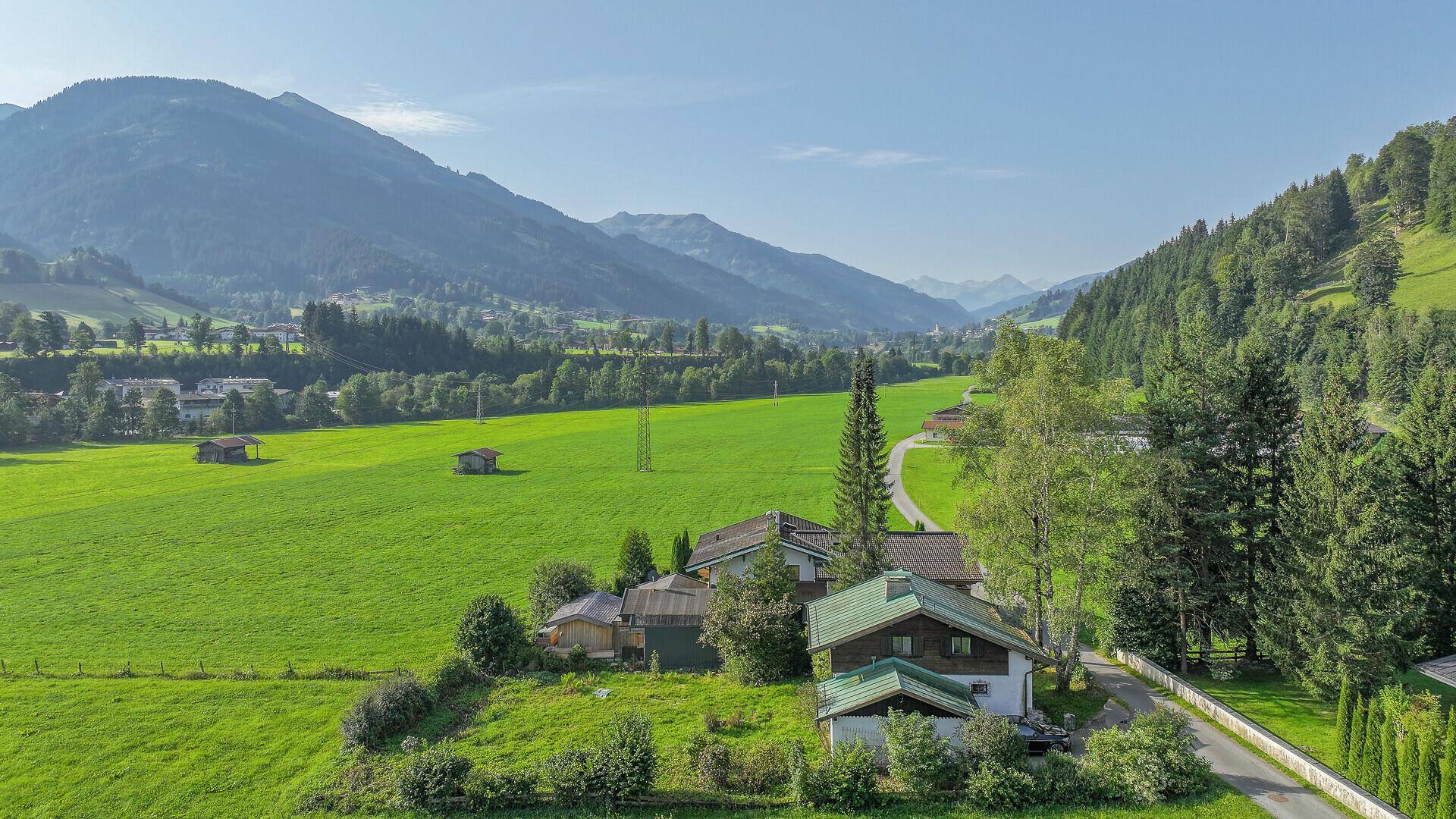 Panoramablick auf das Anwesen in einer malerischen Berglandschaft mit grünen Wiesen und umliegenden Wäldern.