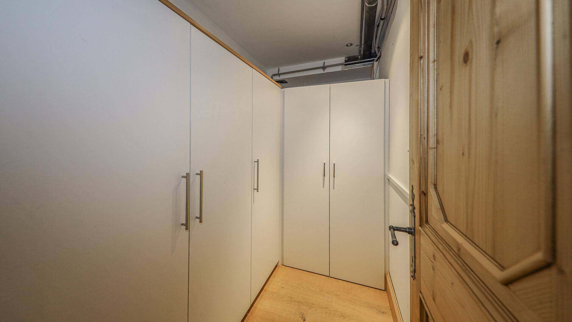 Kleiner Abstellraum mit weißen Einbauschränken und sichtbaren Leitungen an der Decke.