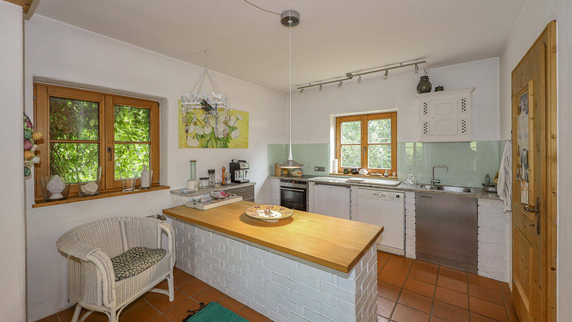 Helle Küche mit Holztheke, Terrakottafliesen und Fenstern mit Blick in den Garten.