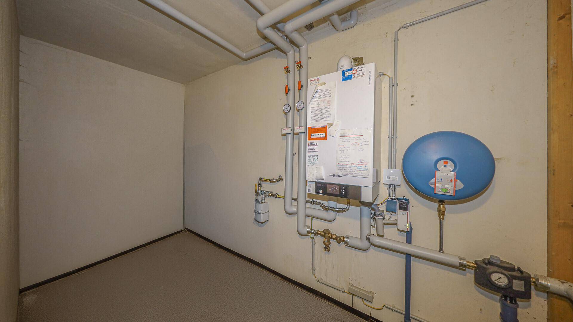 Heizungsraum mit einem modernen Heizkessel und sichtbaren Rohrleitungen an der Wand.