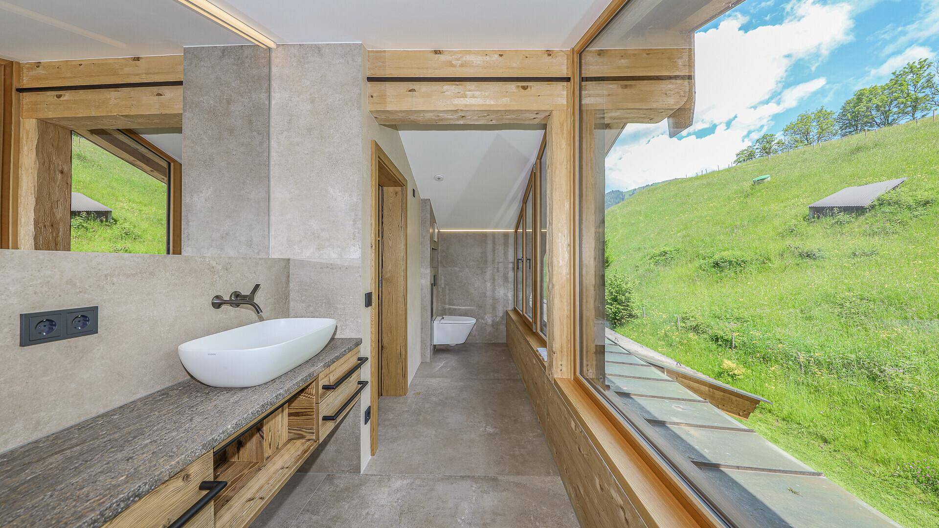 Modernes Badezimmer mit Waschtisch, Wand-WC und großer Fensterfront mit Grünblick.