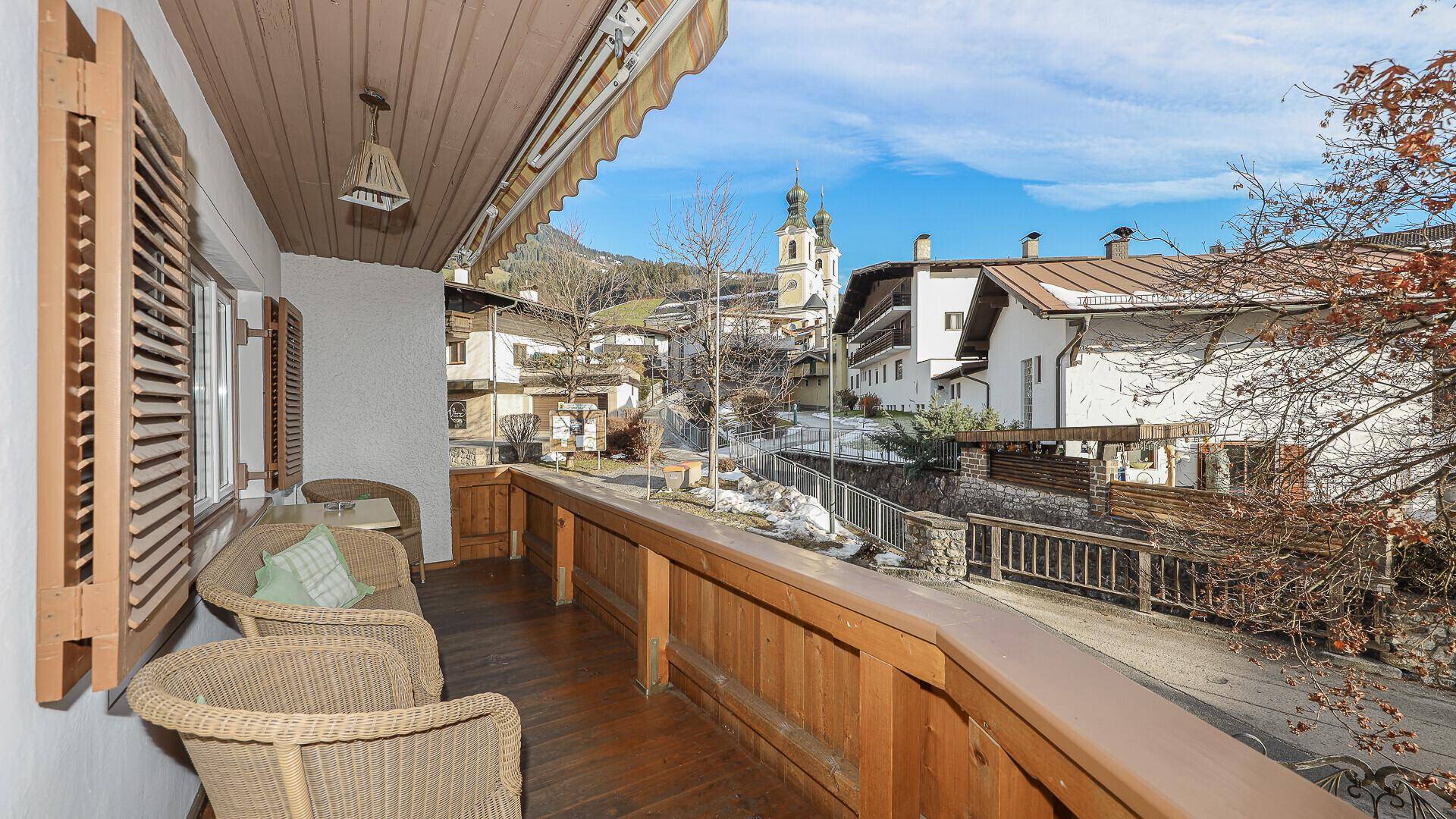Gemütlicher Holzbalkon mit Sitzgelegenheiten und Blick auf das Dorf und die Kirche.