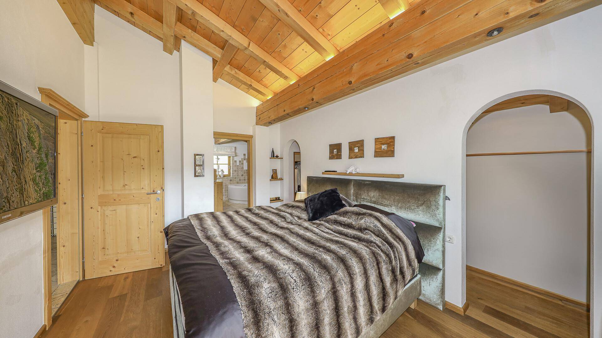 Schlafzimmer mit Holzbalkendecke, Holzboden und offenem Bereich für Kleiderschränke.