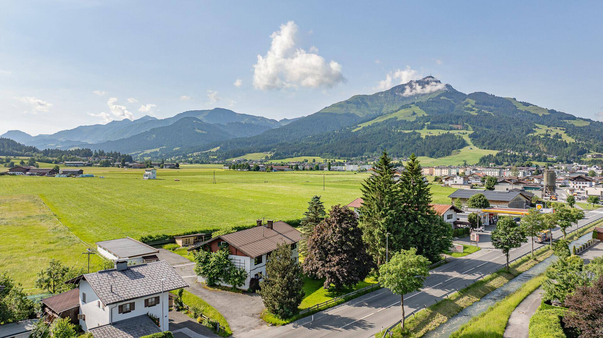 Panoramablick auf die Siedlung mit grünen Wiesen, Bergen und einer klaren Himmelslandschaft.