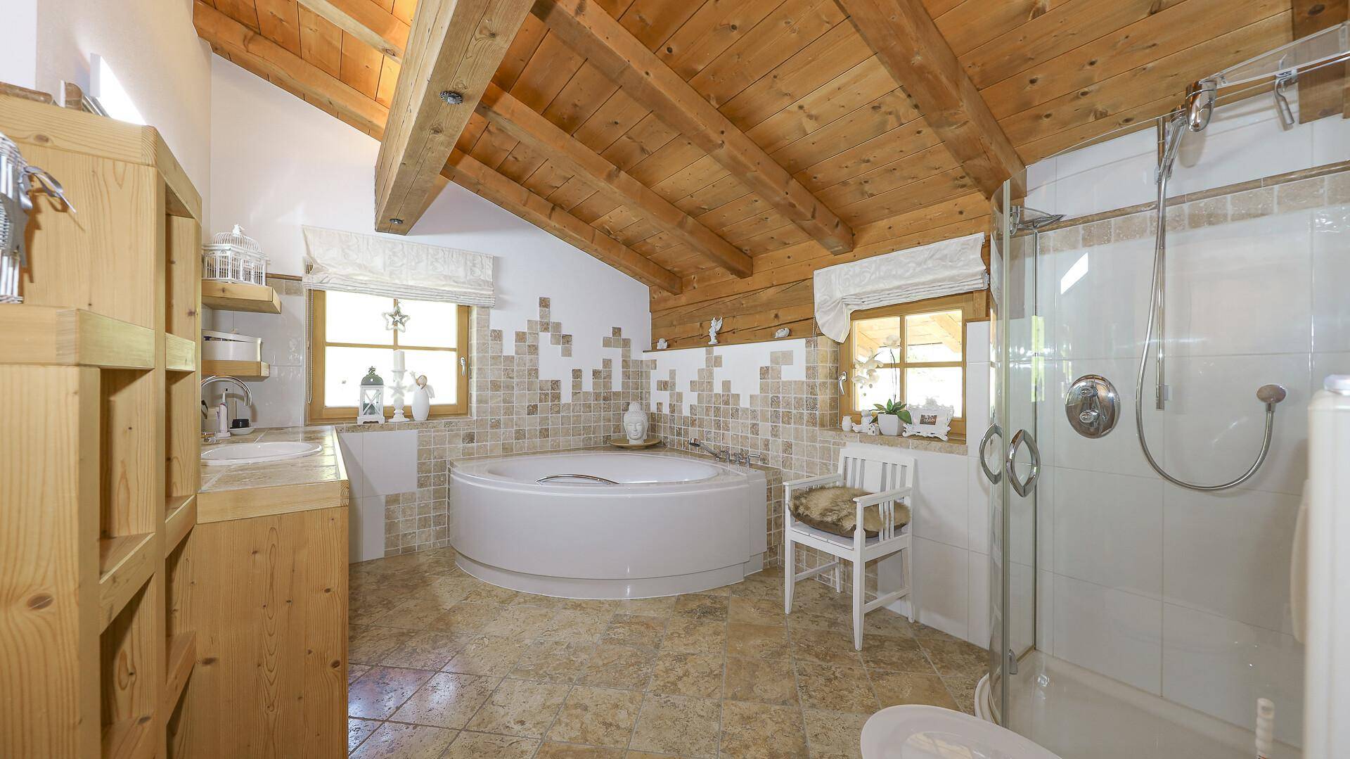 Geräumiges Badezimmer mit runder Badewanne, Dusche, Fliesenboden und Holzbalkendecke.