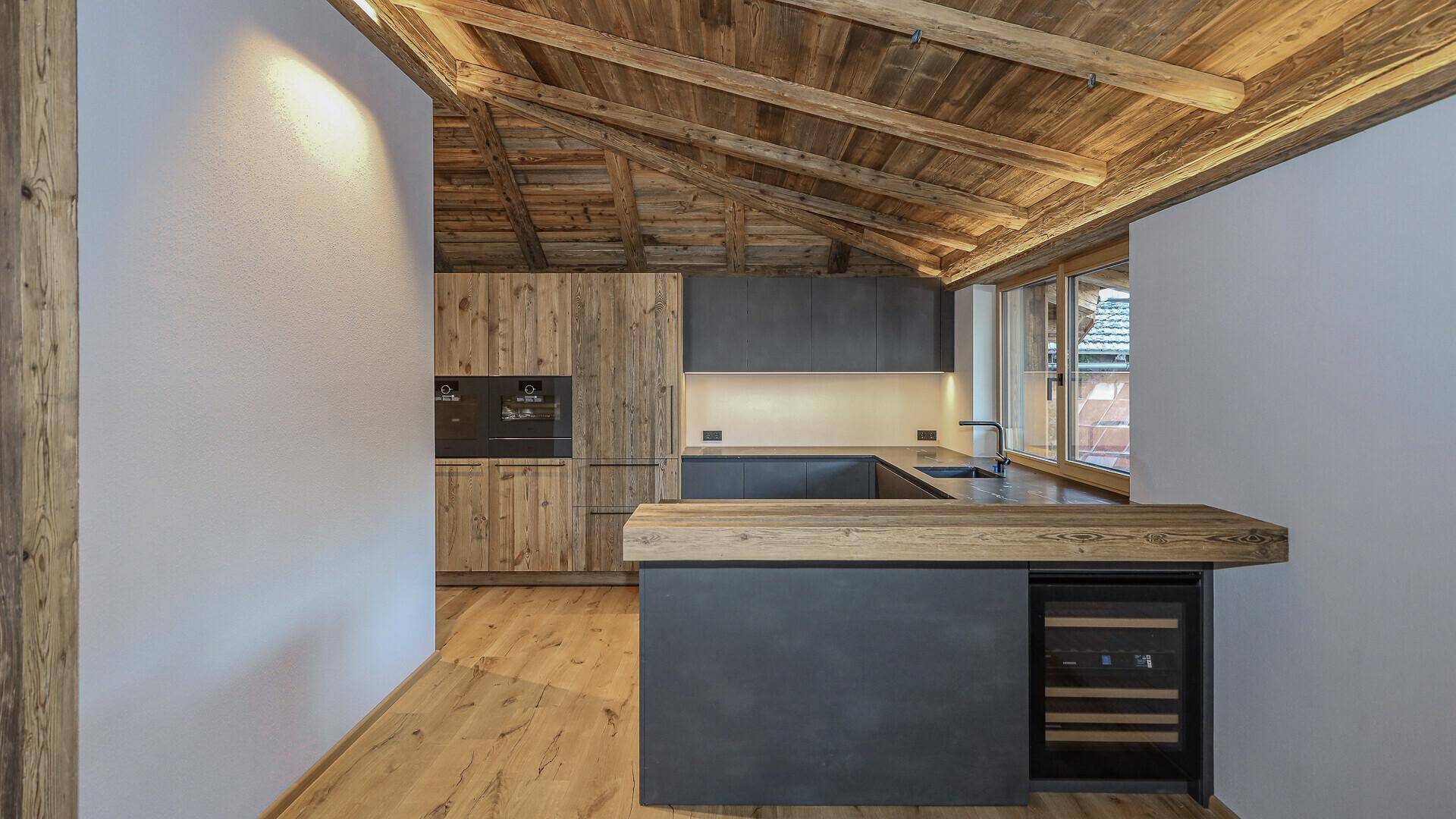 Moderne Küche mit Holzelementen, dunklen Fronten und integriertem Weinkühler.