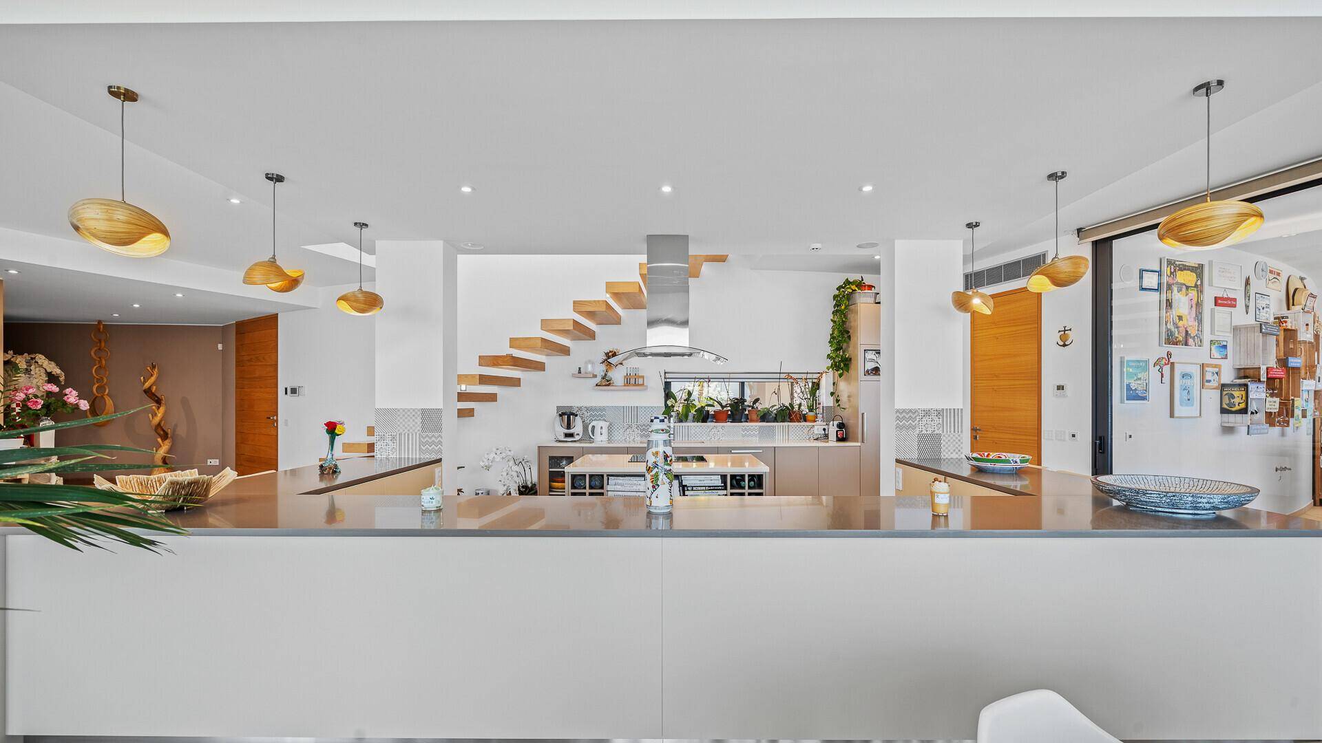Moderne Küche mit langer Theke und Barhockern, offen gestaltet mit Blick auf den Kochbereich und die Treppe.