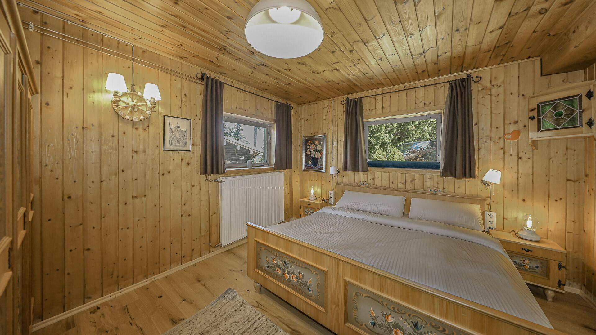 Gemütliches Schlafzimmer mit traditionellem Holzbett, Holztäfelung und Blick ins Grüne.